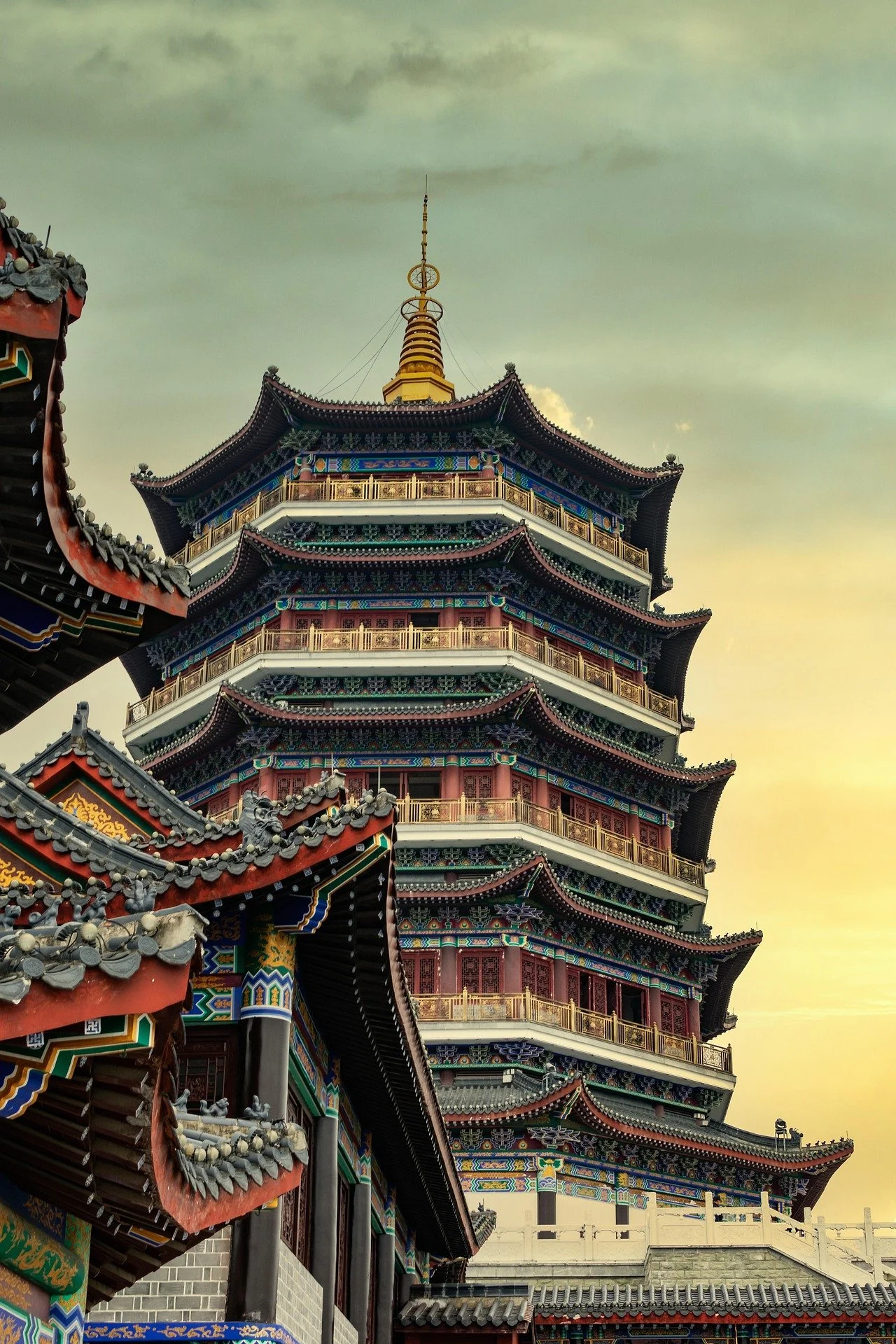 Traditioneller chinesischer Pagodenbau mit mehrstöckigen, geschwungenen Dächern, detailreiche Faserdekorationen und einem goldenen Spitzturm im Hintergrund, bei Sonnenuntergang.