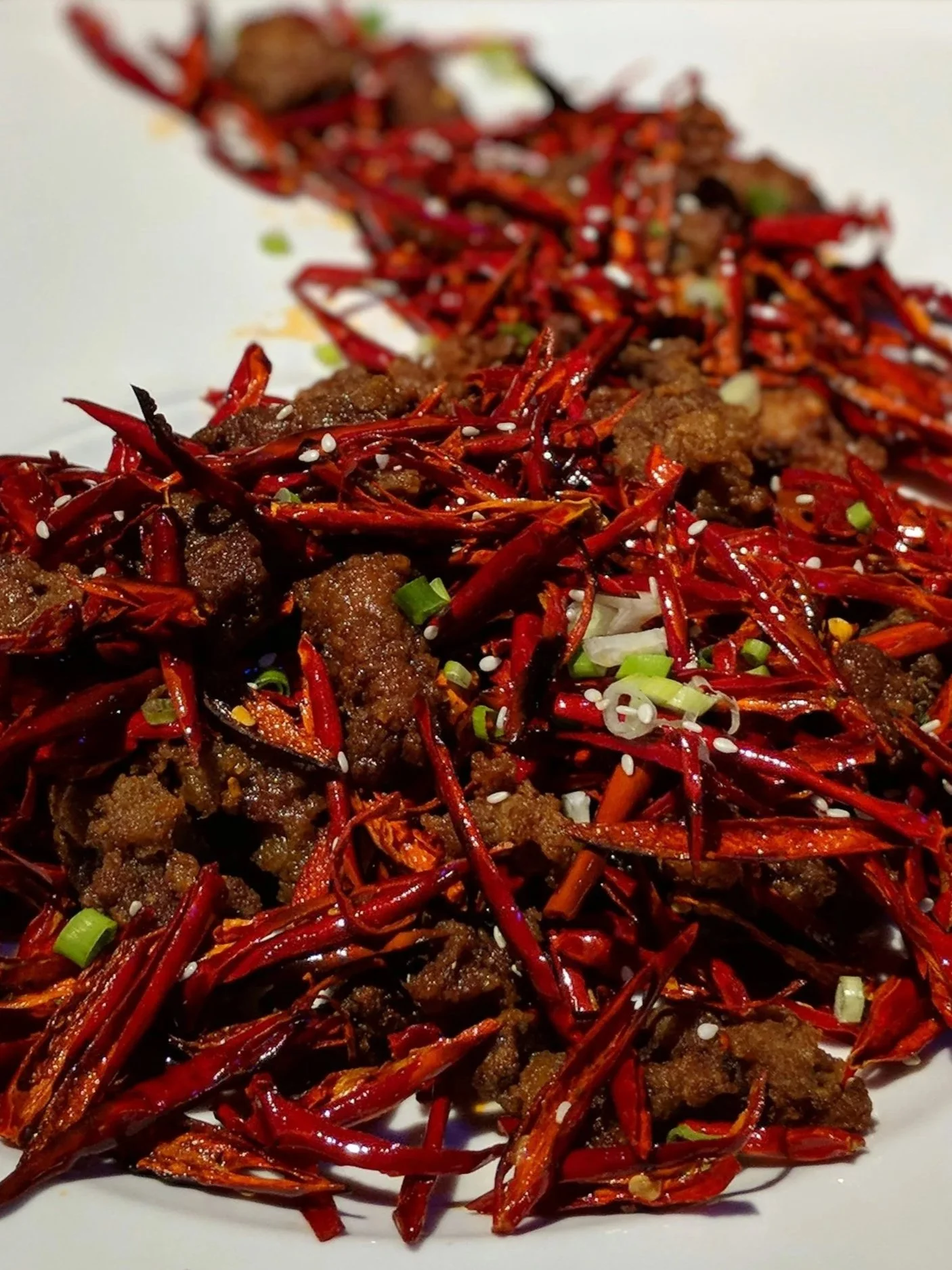 Ein Teller mit würzigem chinesischem Gericht aus gebratenem Fleisch, getrockneten roten Chilis, Frühlingszwiebeln und Sesamsamen.