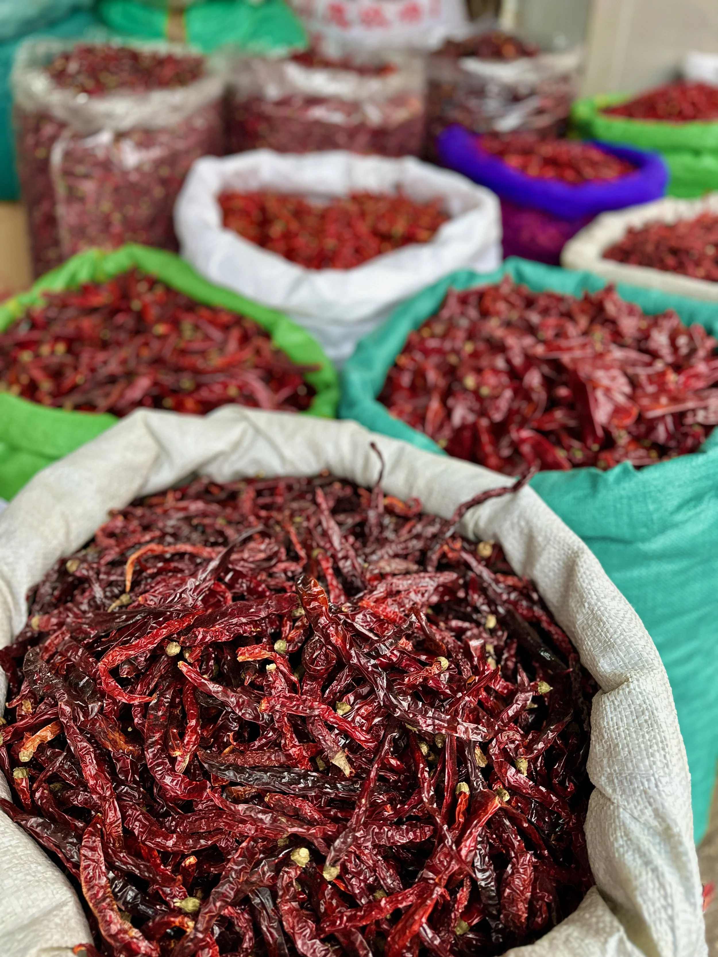 Mehrere Säcke mit roten Chilischoten in einer Markthalle.