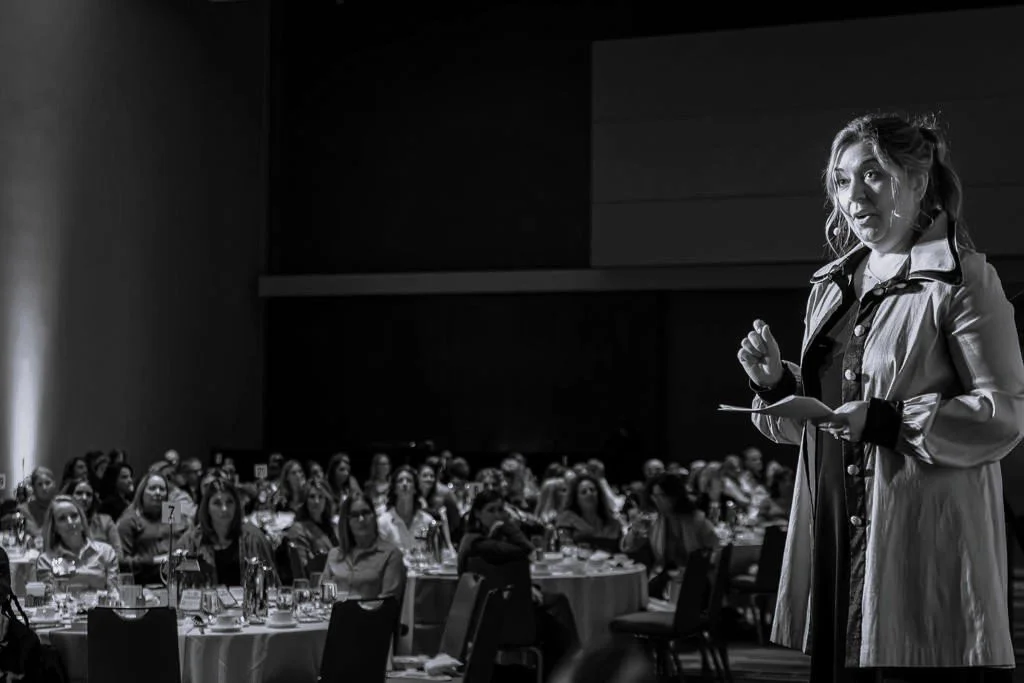 A woman, Andi Campbell, speaking at a conference or event while audience members listen attentively.