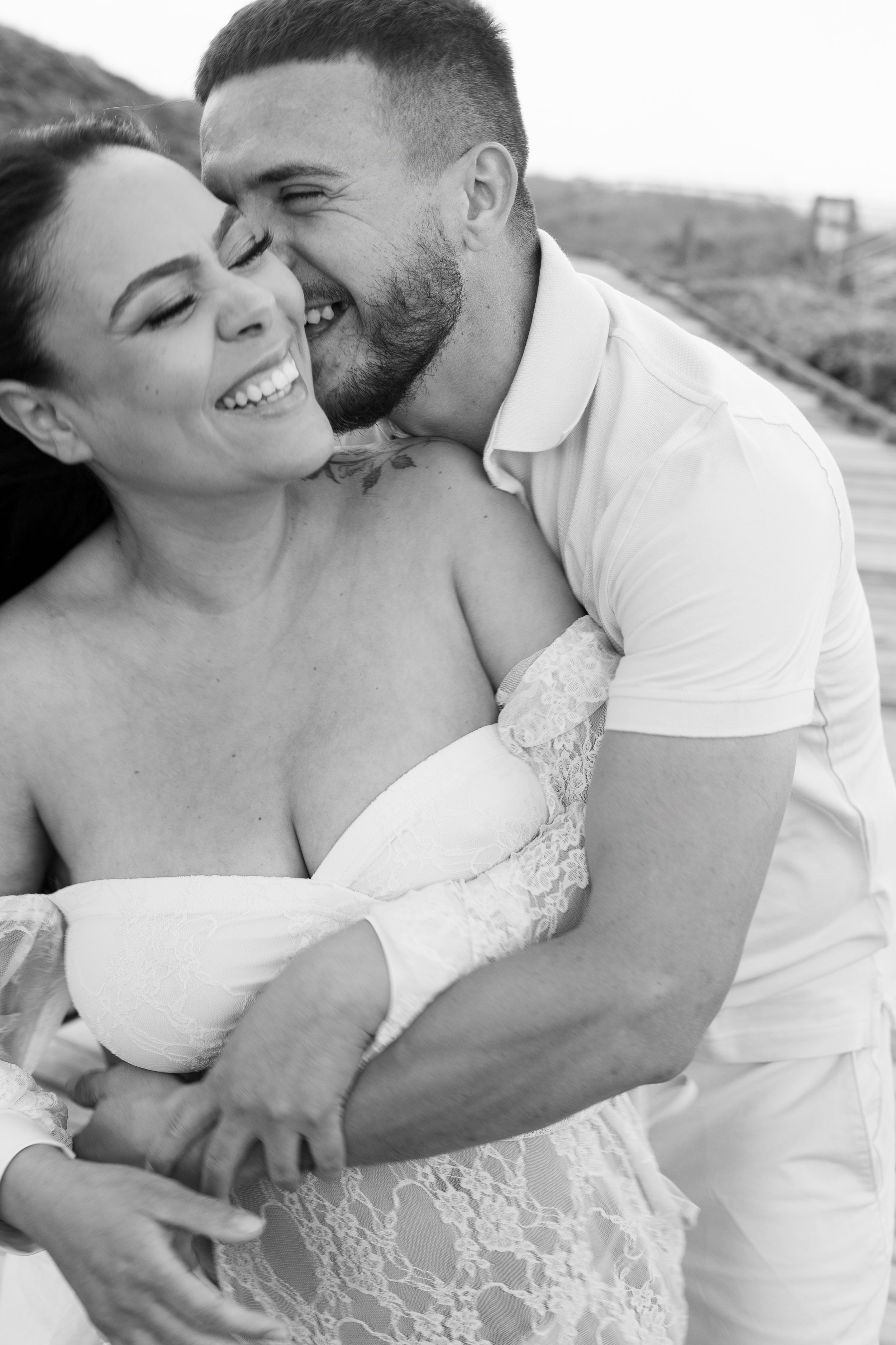 A couple sharing a joyful embrace and kiss on a beach, black and white photo.