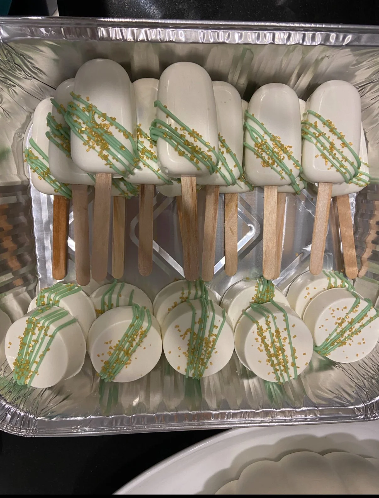 Aluminum tray with white popsicles decorated with green drizzle and yellow sprinkles.