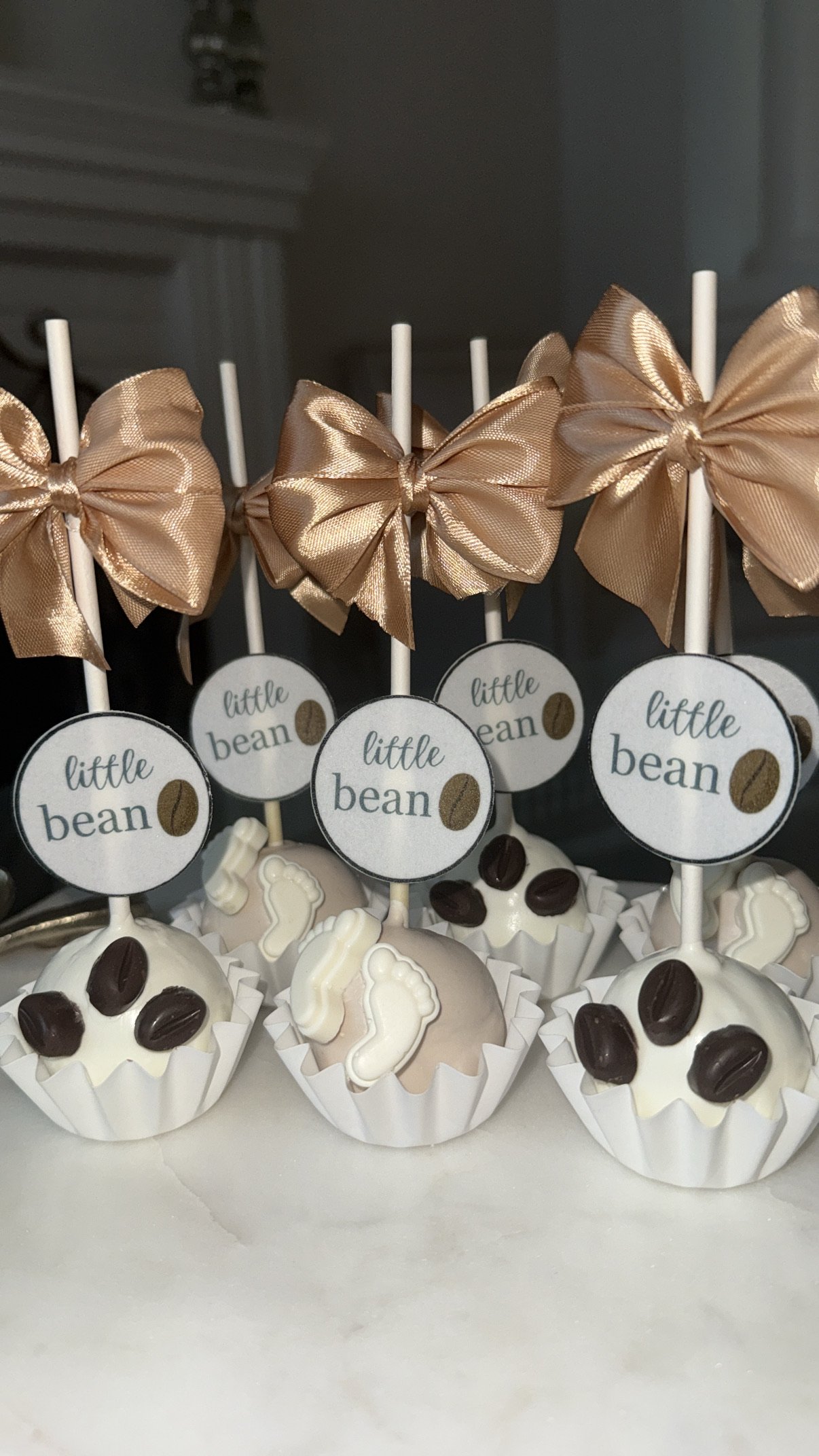 Valentine's Day-themed desserts on a white marble table at a restaurant, including cupcakes topped with pink flowers, white frosted cakes on a cake stand, and heart-shaped cookies with pink flowers.