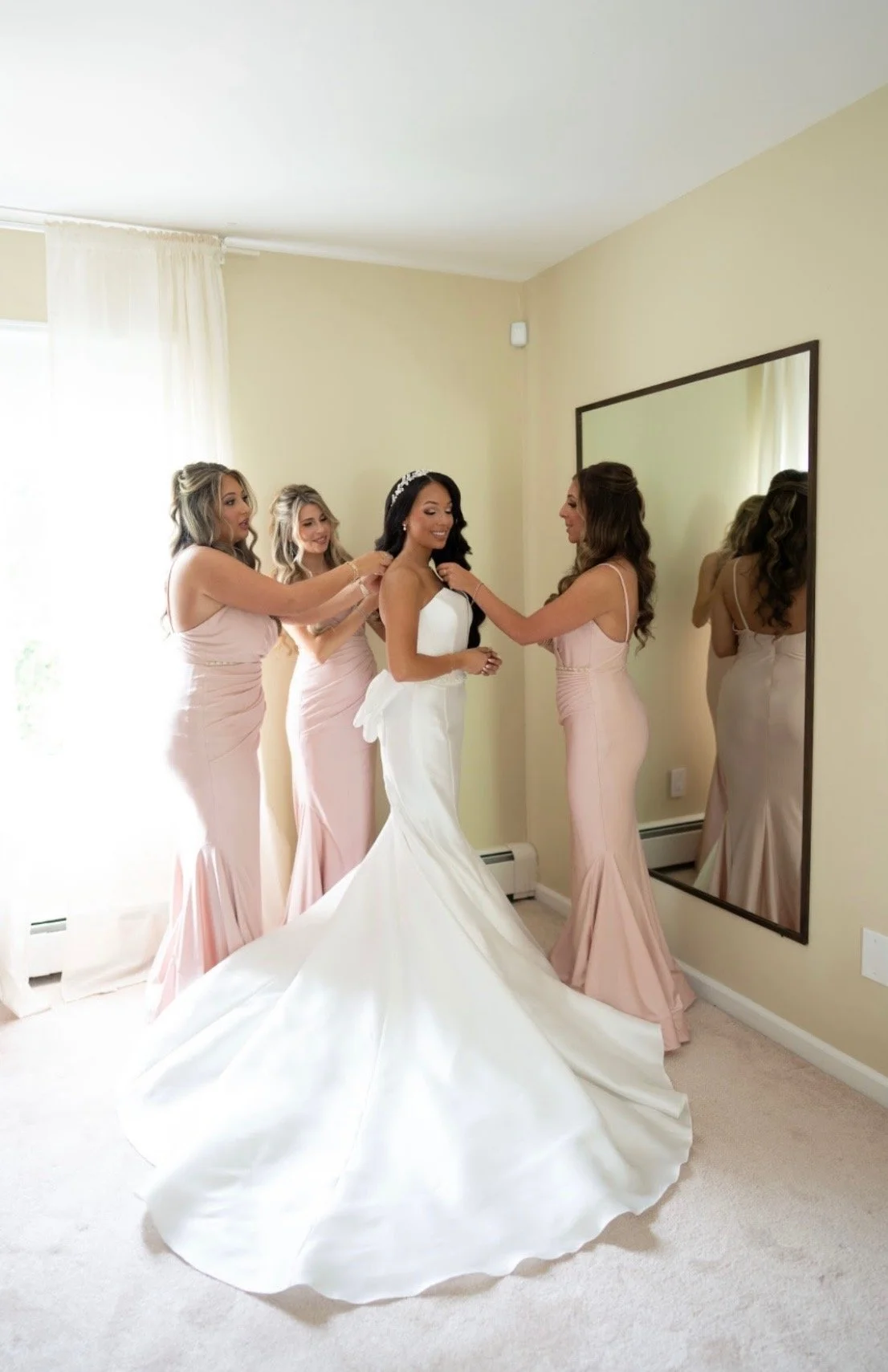 Bride getting ready with her bridesmaids in a room before her wedding.