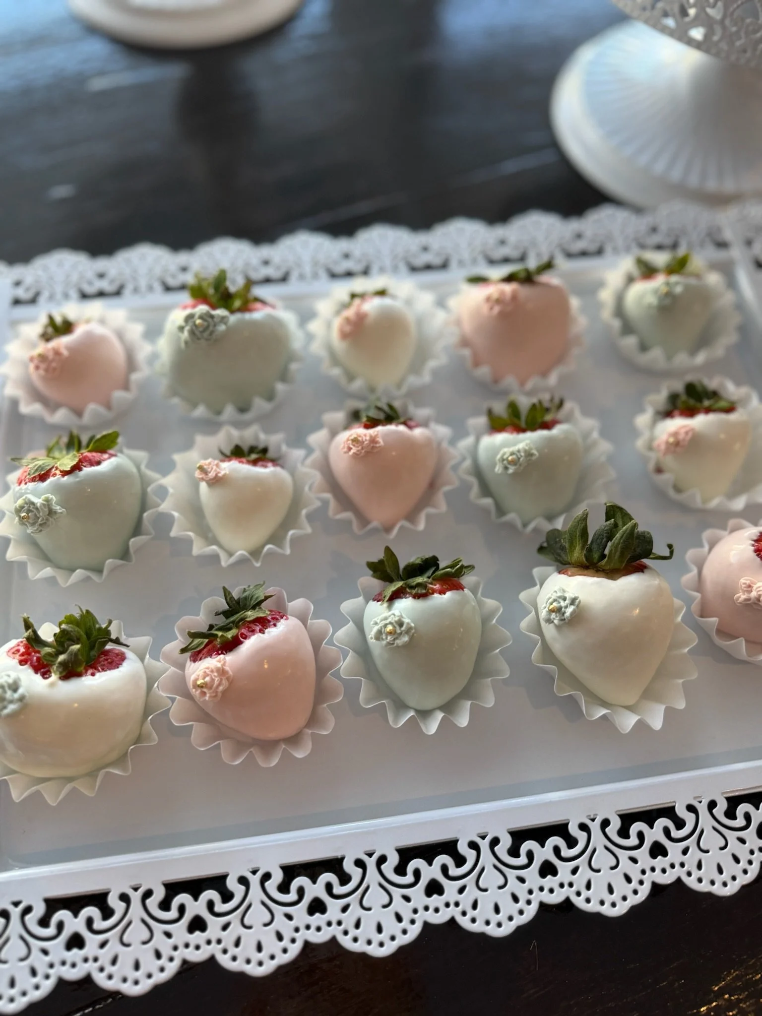 Cupcakes decorated with pink frosting, white sugar flowers, and pearl sprinkles on a gold decorative cake stand with hanging crystal accents.