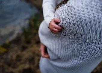 Close-up of a child hugging an adult, with both wearing knit sweaters, near a river or pond.
