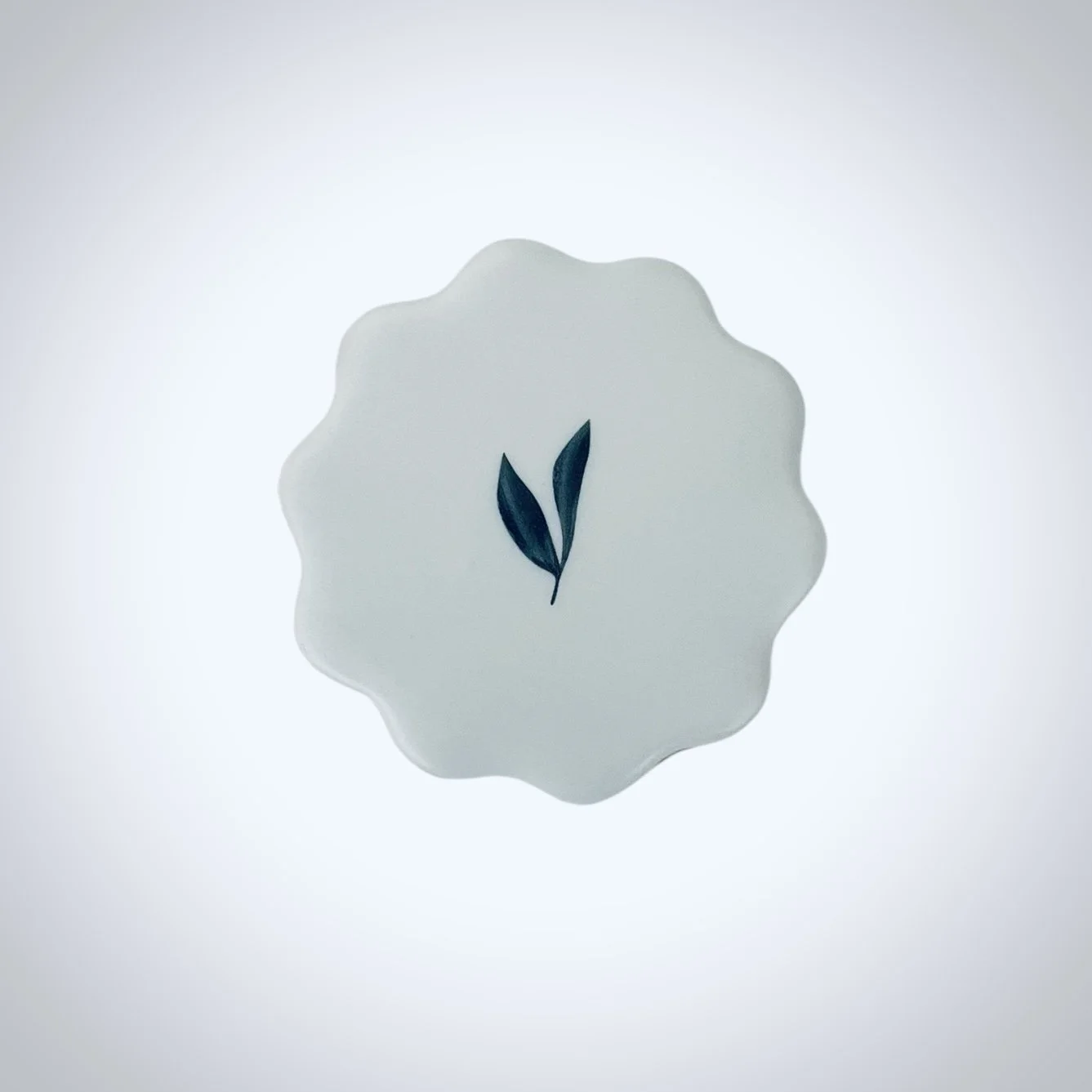 Round scalloped cookie printed with minimal botanical leaf design on white icing designed for corporate retreat favors and client gifting. Photographed on a white background.