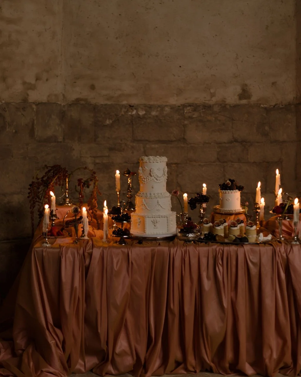 Romantic luxury dessert tablescape featuring ruched pink satin, vintage silverware, and warm candlelight ambiance