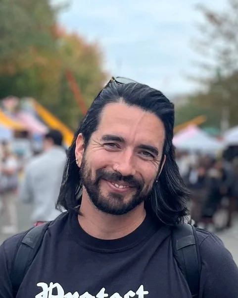 A man smiling with a t-shirt on reading 'protect trans kids'