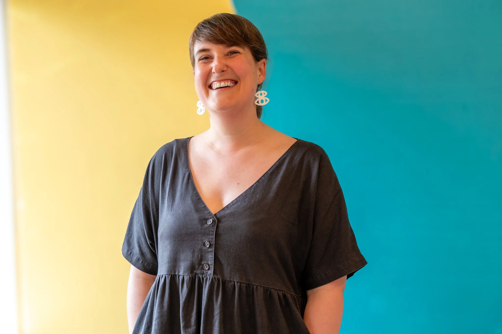 A young woman with short brown hair smiling and holding up a black poster board decorated with a galaxy pattern and a small white ghost illustration.