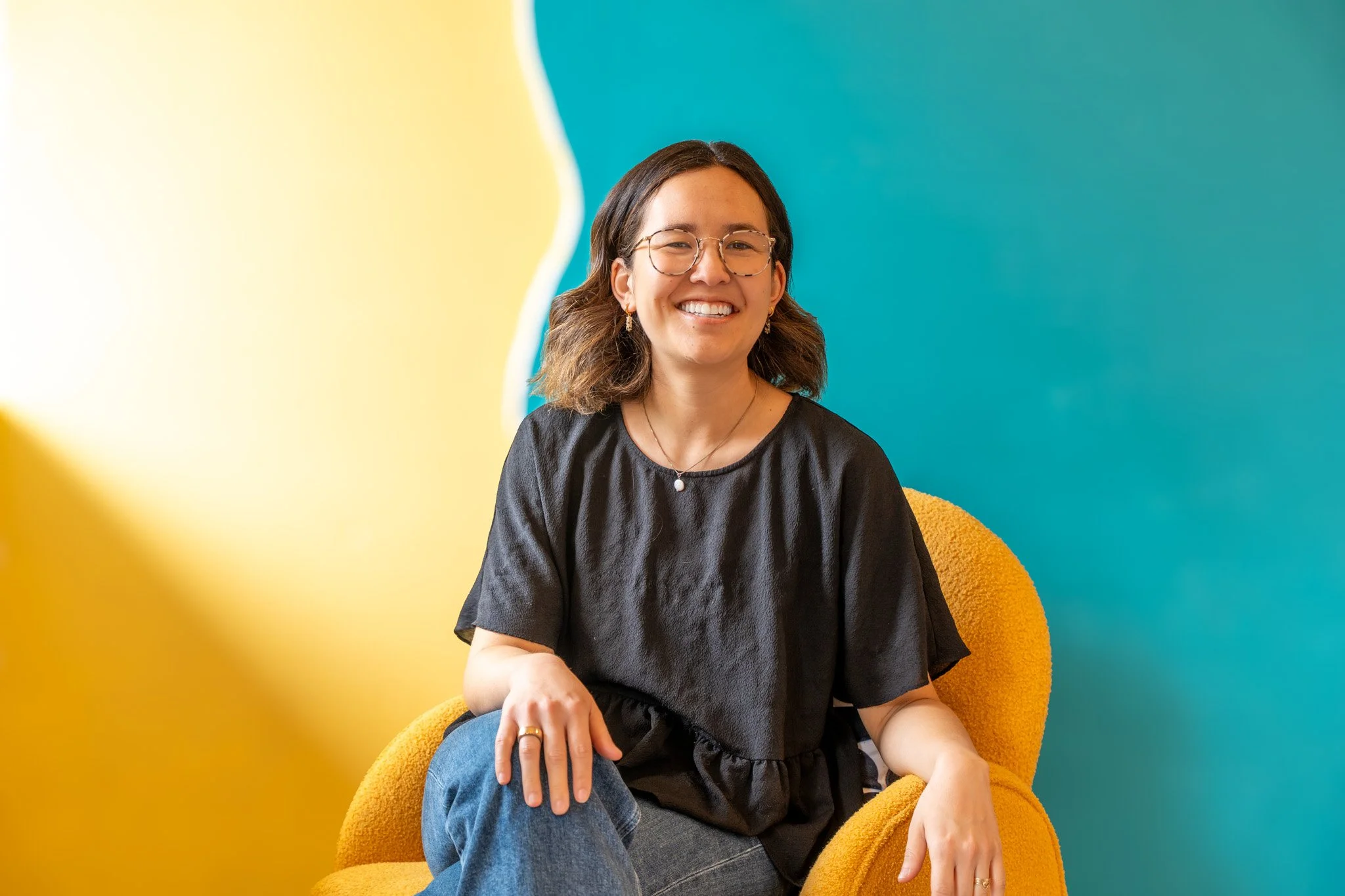 Young woman with glasses smiling outdoors with a lighthouse in the background.