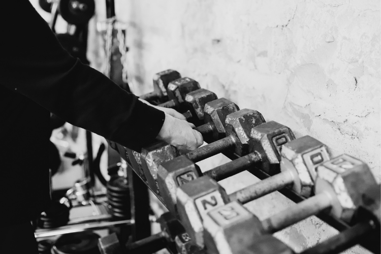 A person adjusting or lifting a row of dumbbells on a rack in a gym.