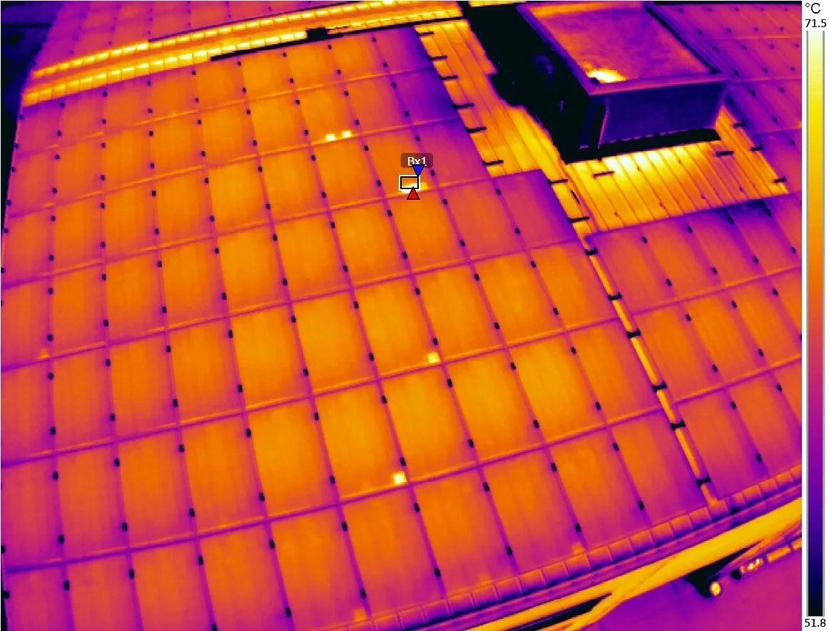 Infrared image of a rooftop showing heat variation, with a small structure on the roof and a grid of solar panels.