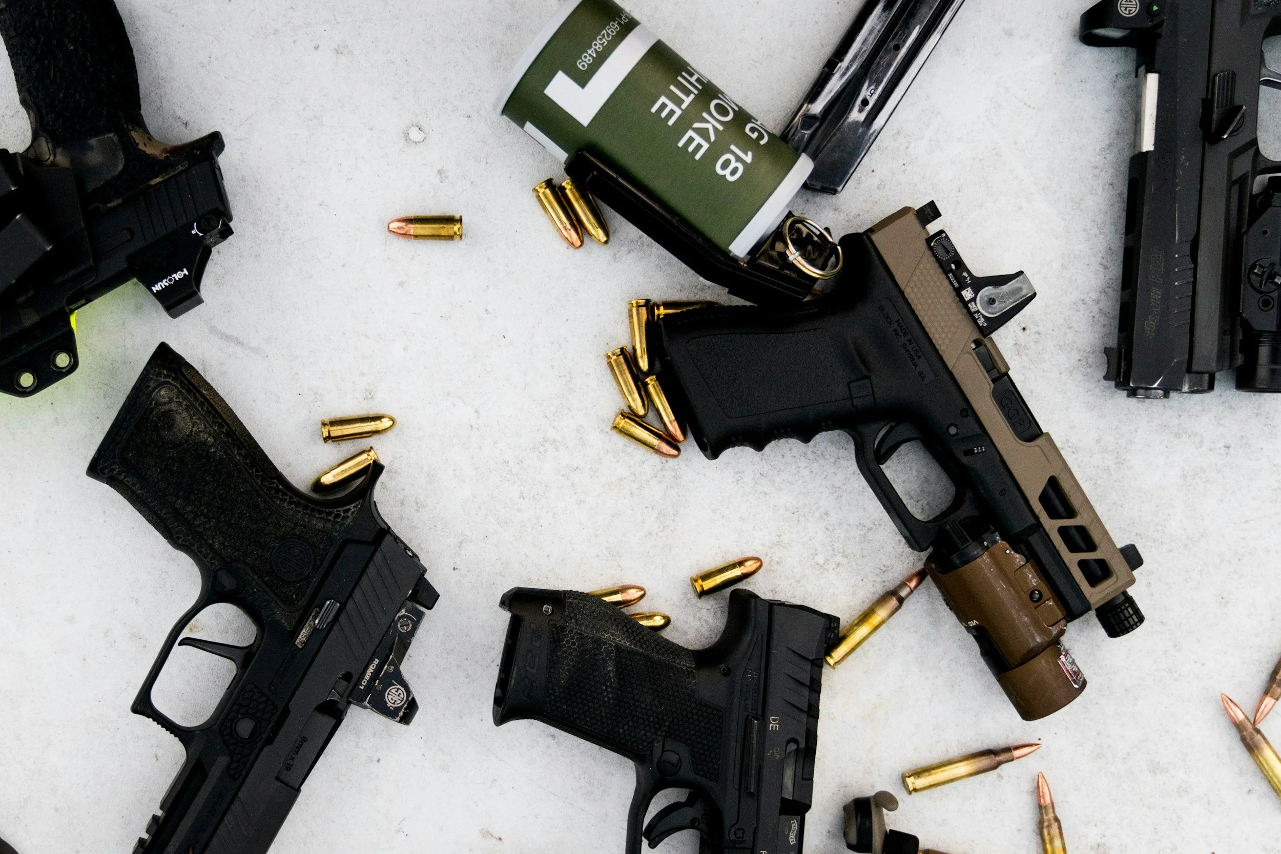 Several handguns, bullets, and gun accessories scattered on a light gray surface.
