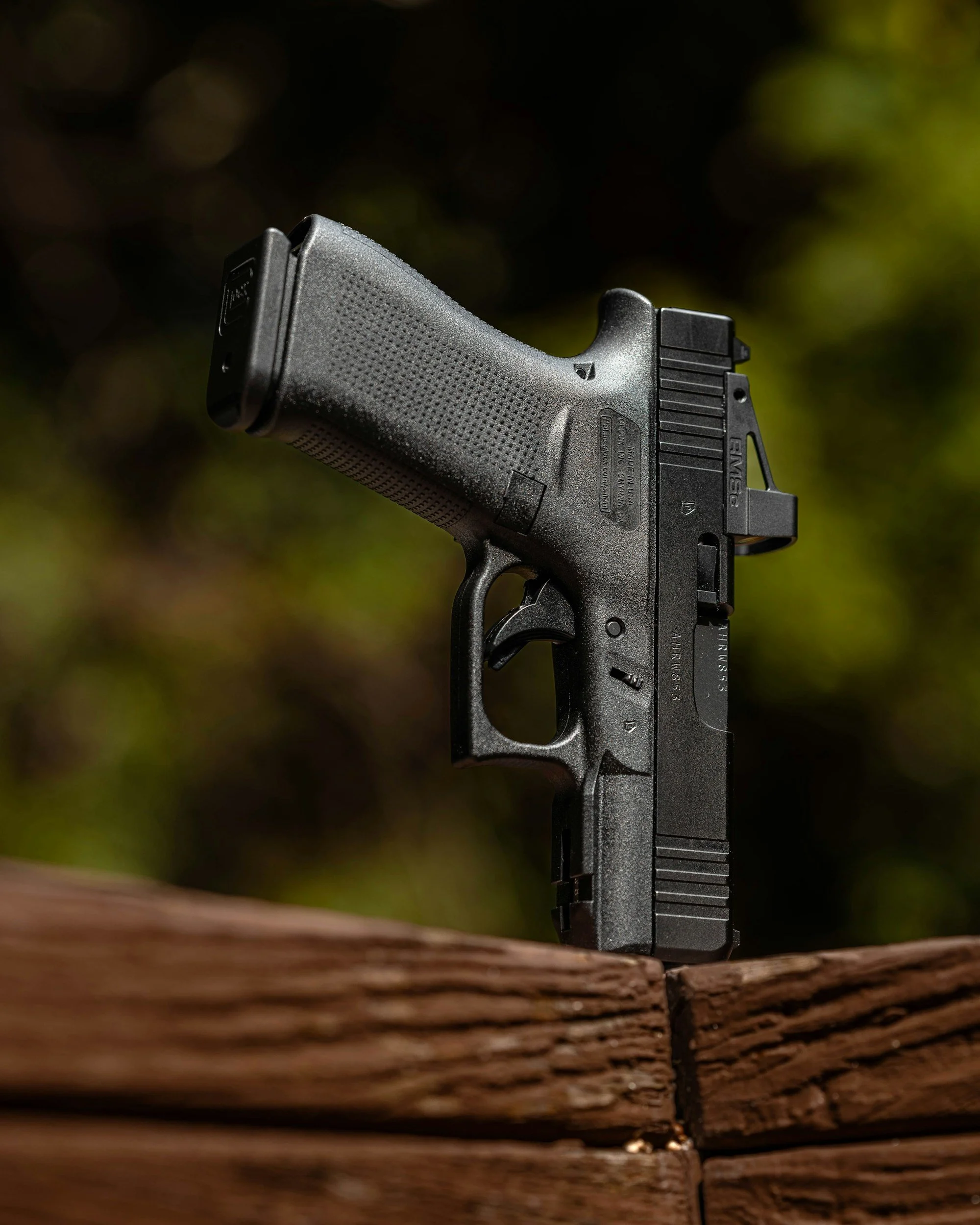 A black handgun resting on a wooden surface with a blurred natural background.