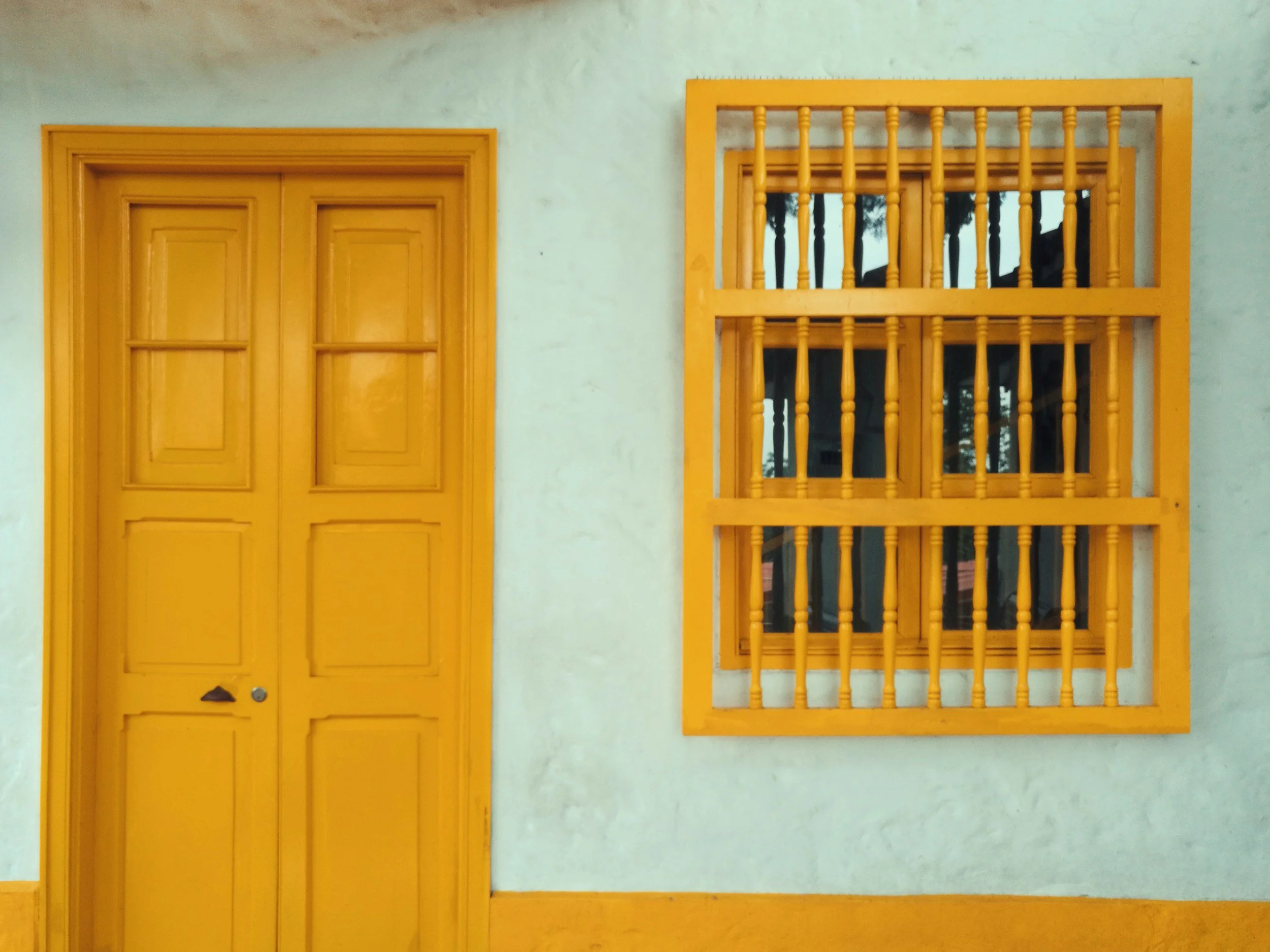 Puerta y ventana con barrotes pintados de color amarillo en una pared de color blanco.