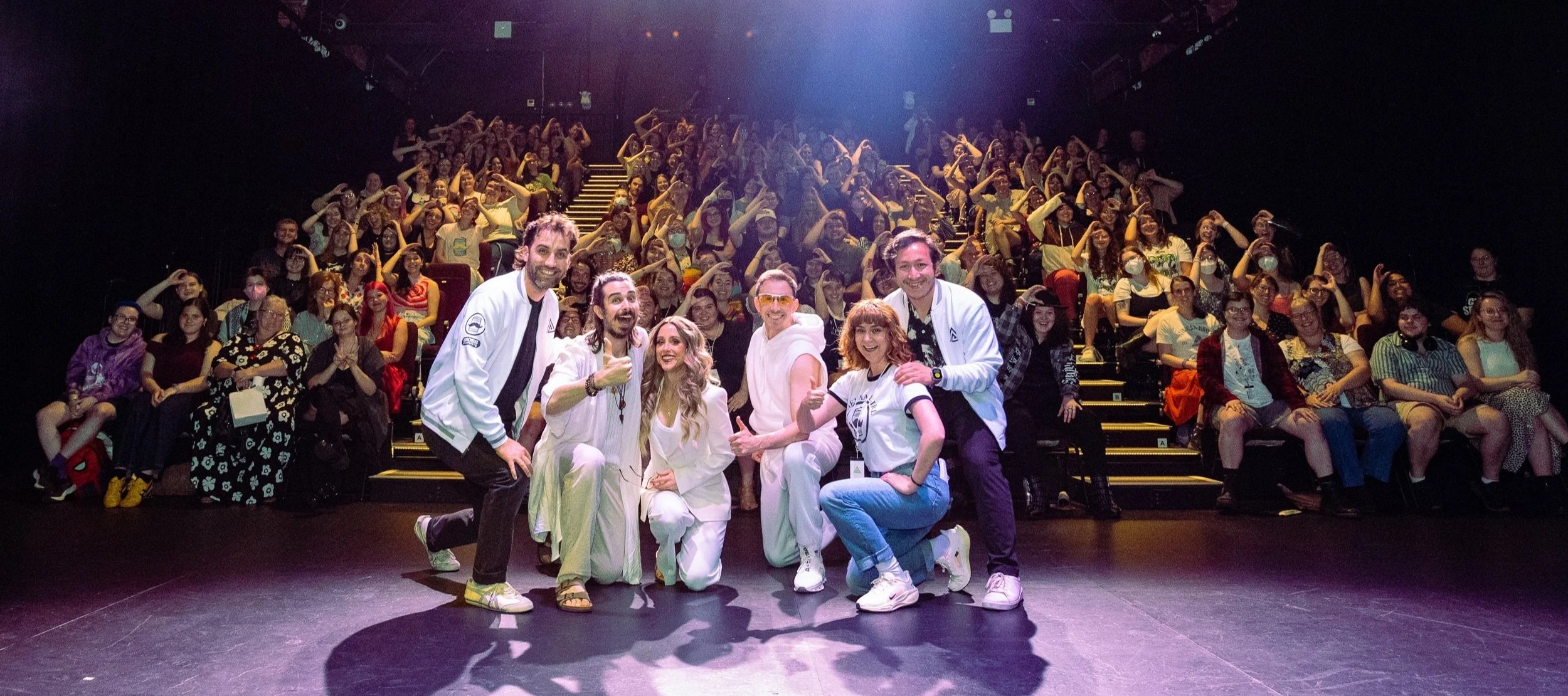 Brian, the owner of Make The Damn Show, a tool kit to make your own theater show, stands on stage with his cast with the audience smiling in the background of theshow Gross Prophets he starred in and produced