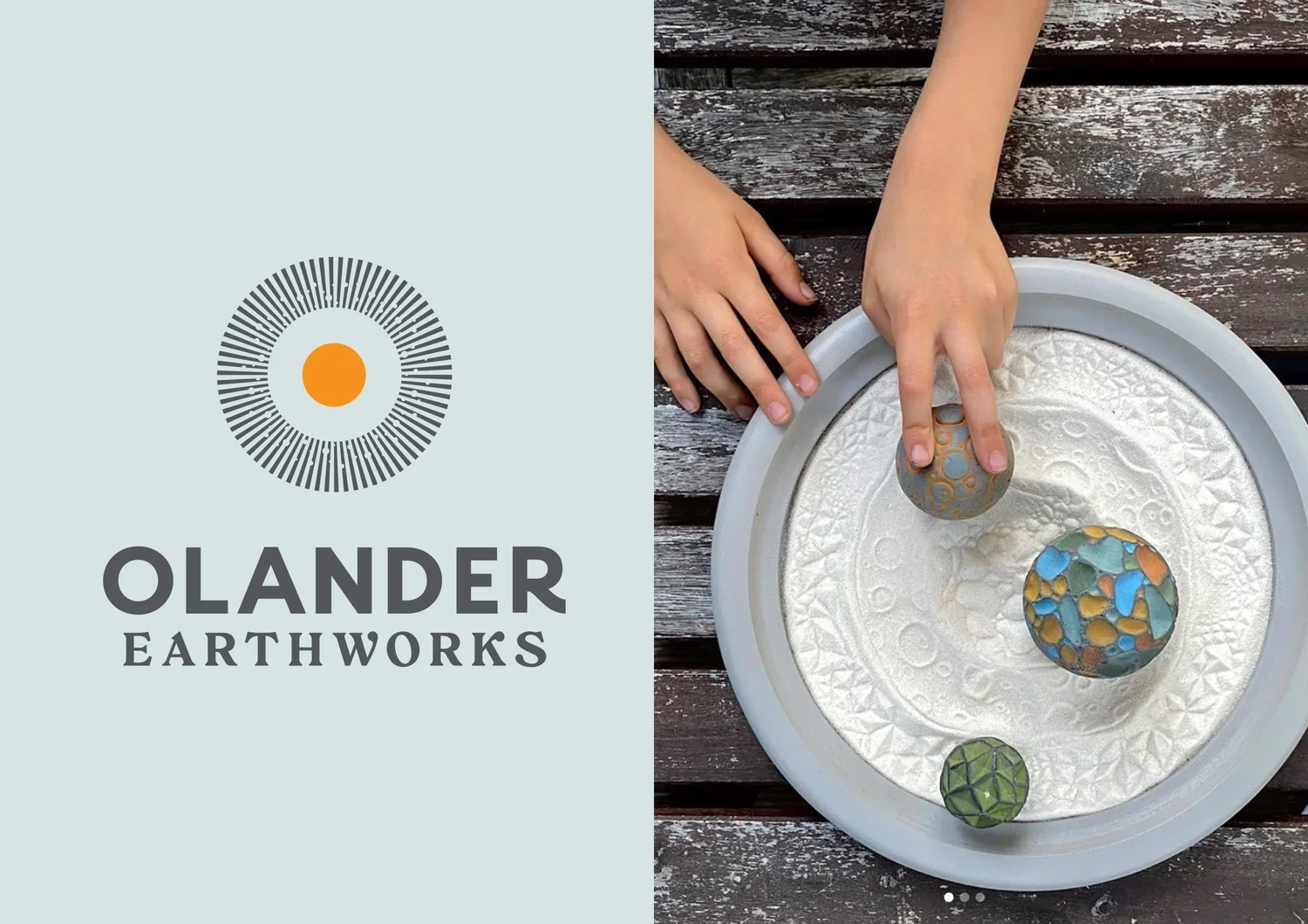 A person using a stone to smooth a painted rock on a white tray filled with white sand, with a rustic wooden surface underneath.