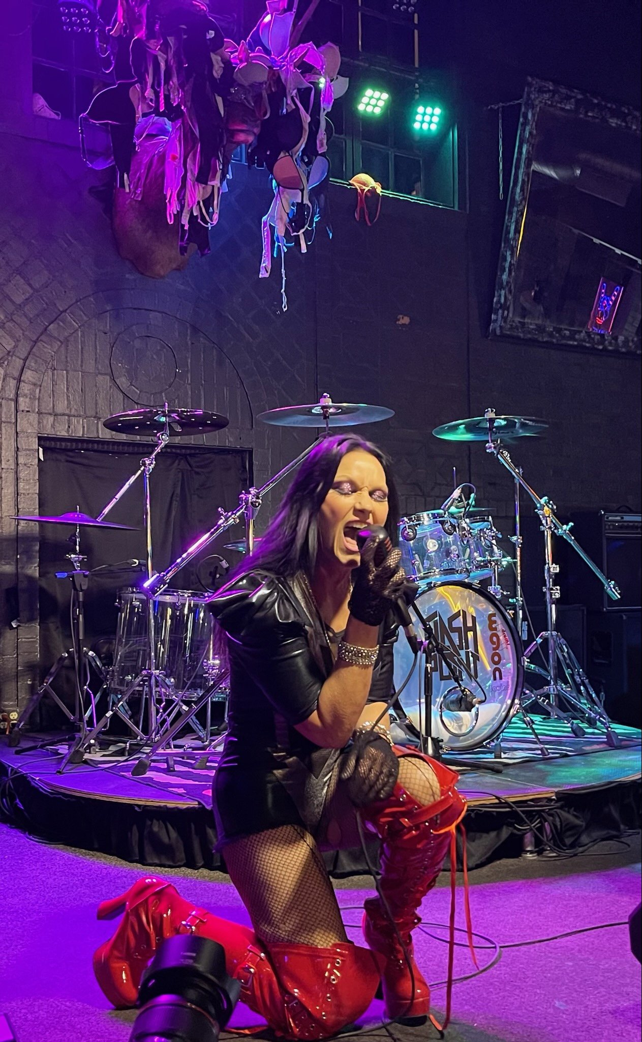 Danielle Bloom-The Virago performing live on stage in red boots and black leather, mid-scream under stage lights.