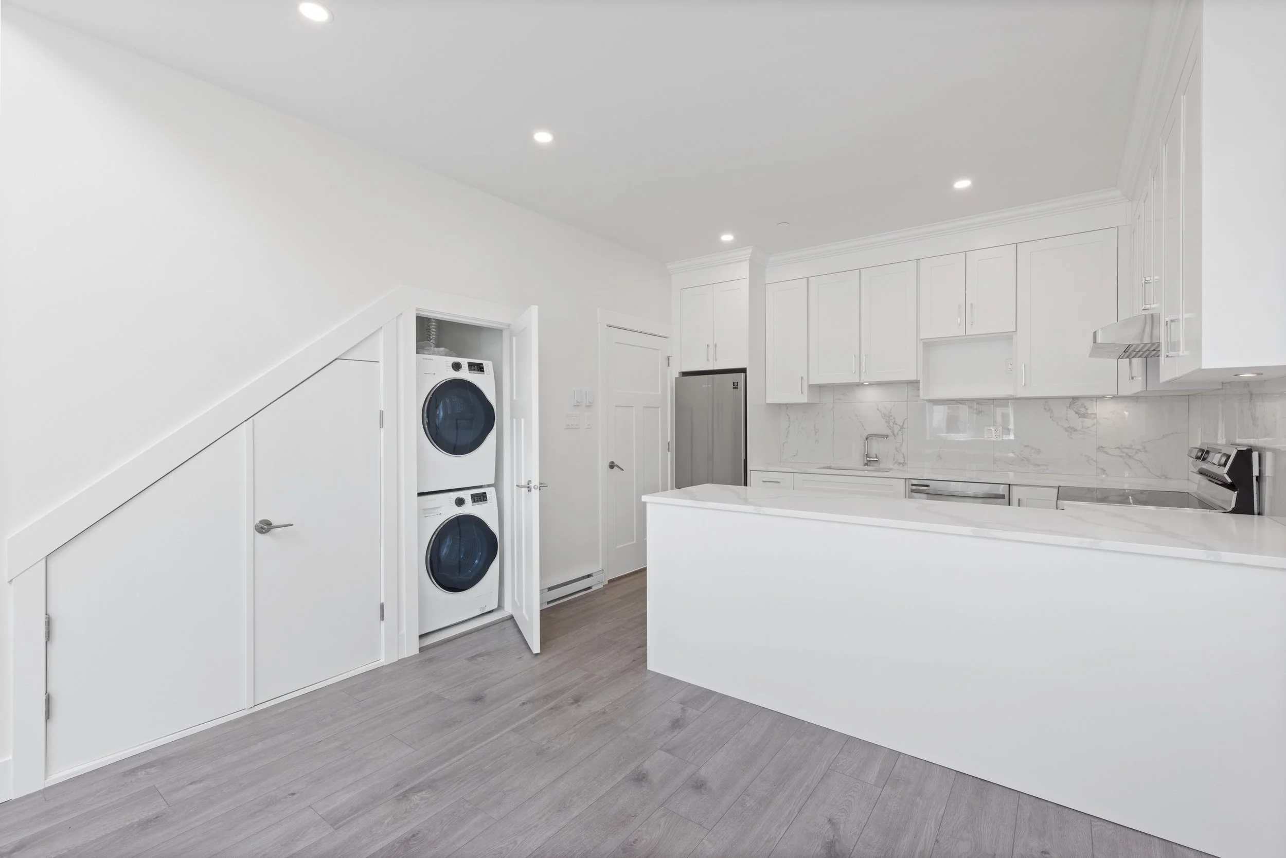 Modern kitchen with white cabinets, marble backsplash, stainless steel appliances, and a stacked washer and dryer concealed behind closed doors.