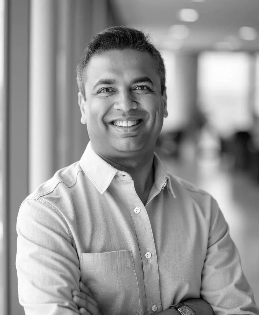 Smiling, confident, entrepreneurial man with glasses and a smartwatch, standing with arms crossed in front of a geometric patterned background