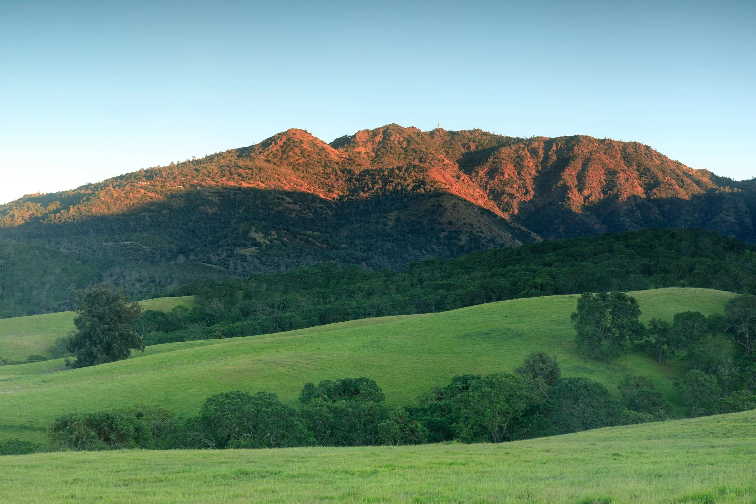 Sunset illuminating a mountain range with green valleys below.