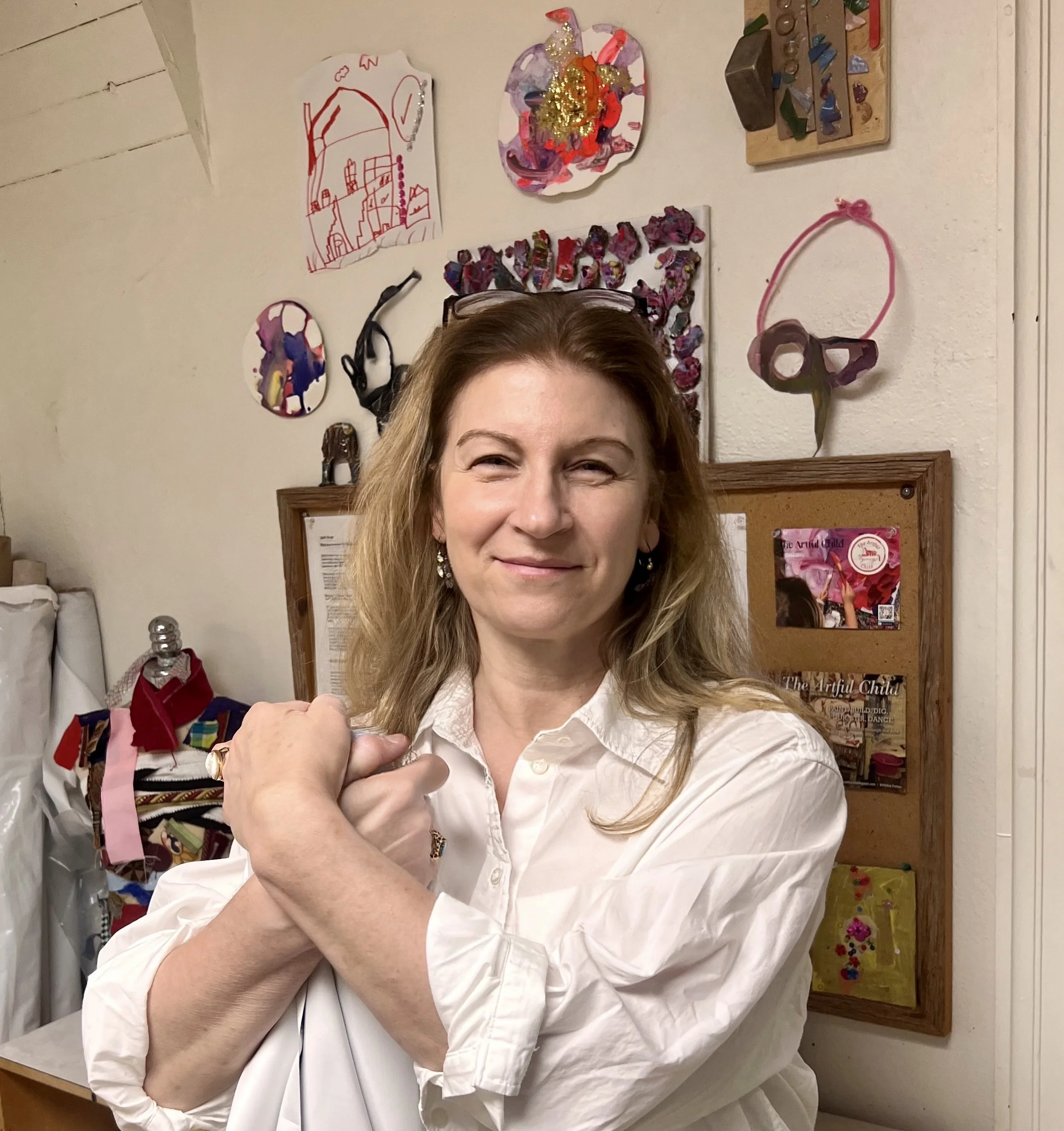 A woman smiling and making a fist in a room decorated with colorful art and crafts displayed on the wall.