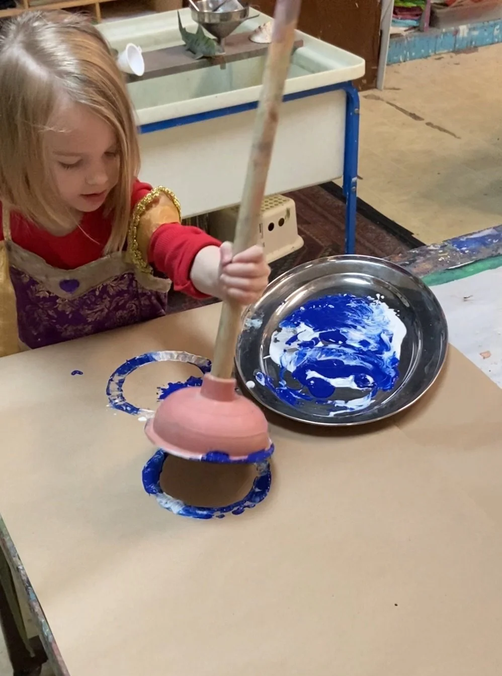 A young girl with blonde hair painting a ceramic object with blue and white paint in an art studio.