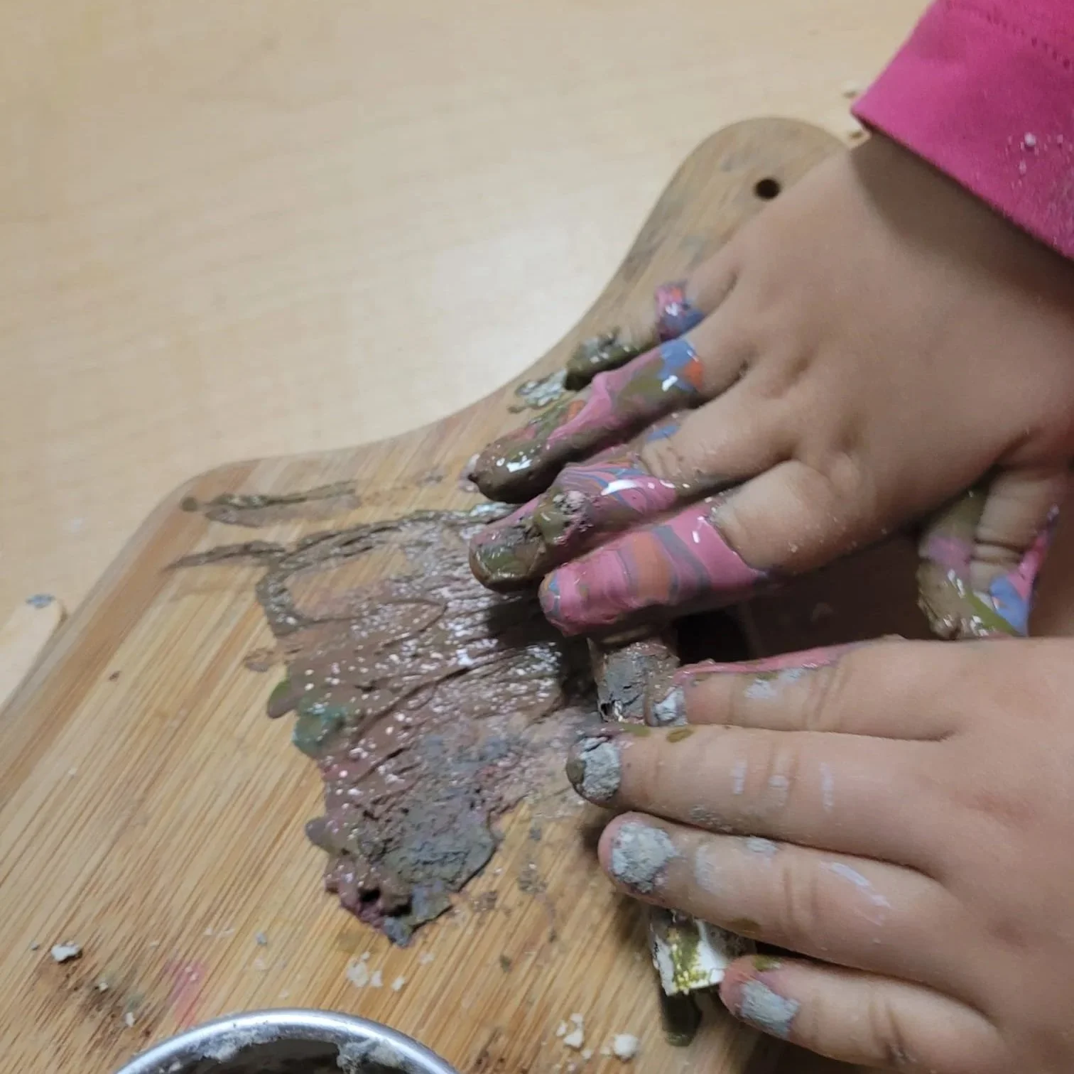 Child's hands pressing and kneading colorful clay or playdough on a wooden surface.