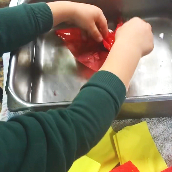 Preschool child exploring red and yellow tissue paper in a metal tray during an open-ended process art experience