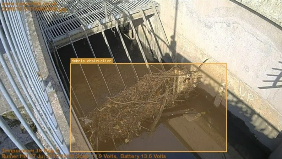 A drainage grate with debris and obstructions blocking water flow, with a warning overlay labeled 'debris obstruction'.