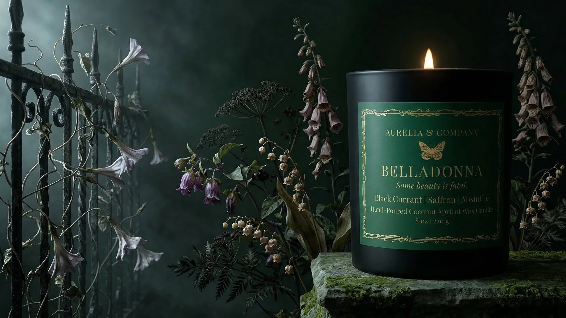 A black candle with a gold and green label surrounded by dried flowers and plants on a moss-covered surface, set against a dark background.
