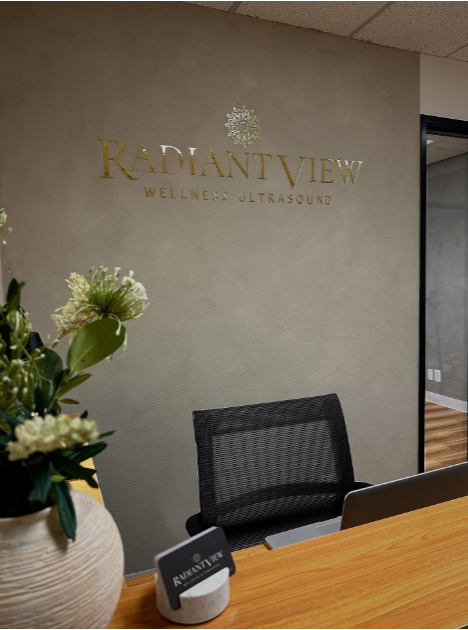 Interior of Radiant View Wellness Ultrasound reception area with a reception desk, an office chair, a plant, and a sign on the wall.