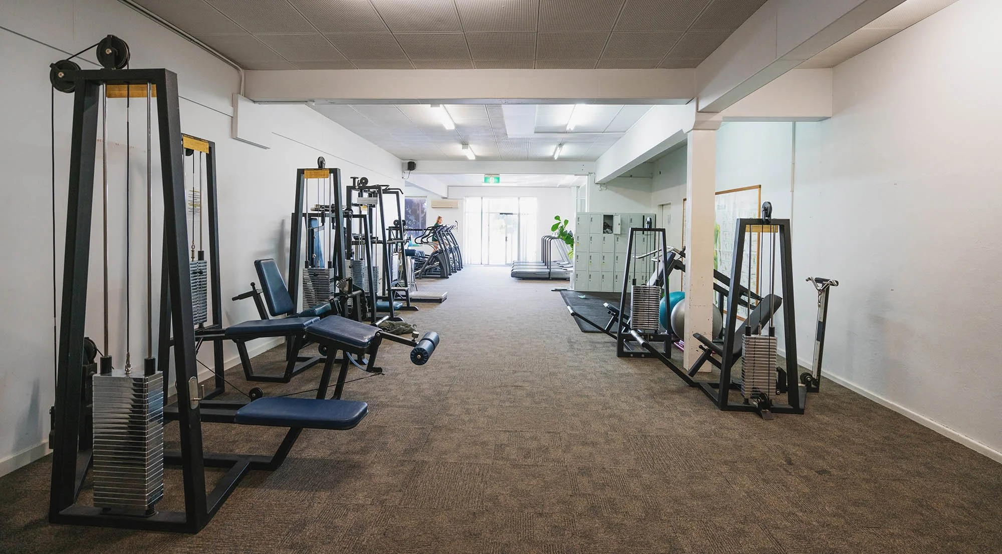 Empty gym room with various exercise equipment like weight machines, treadmills, and stability balls.