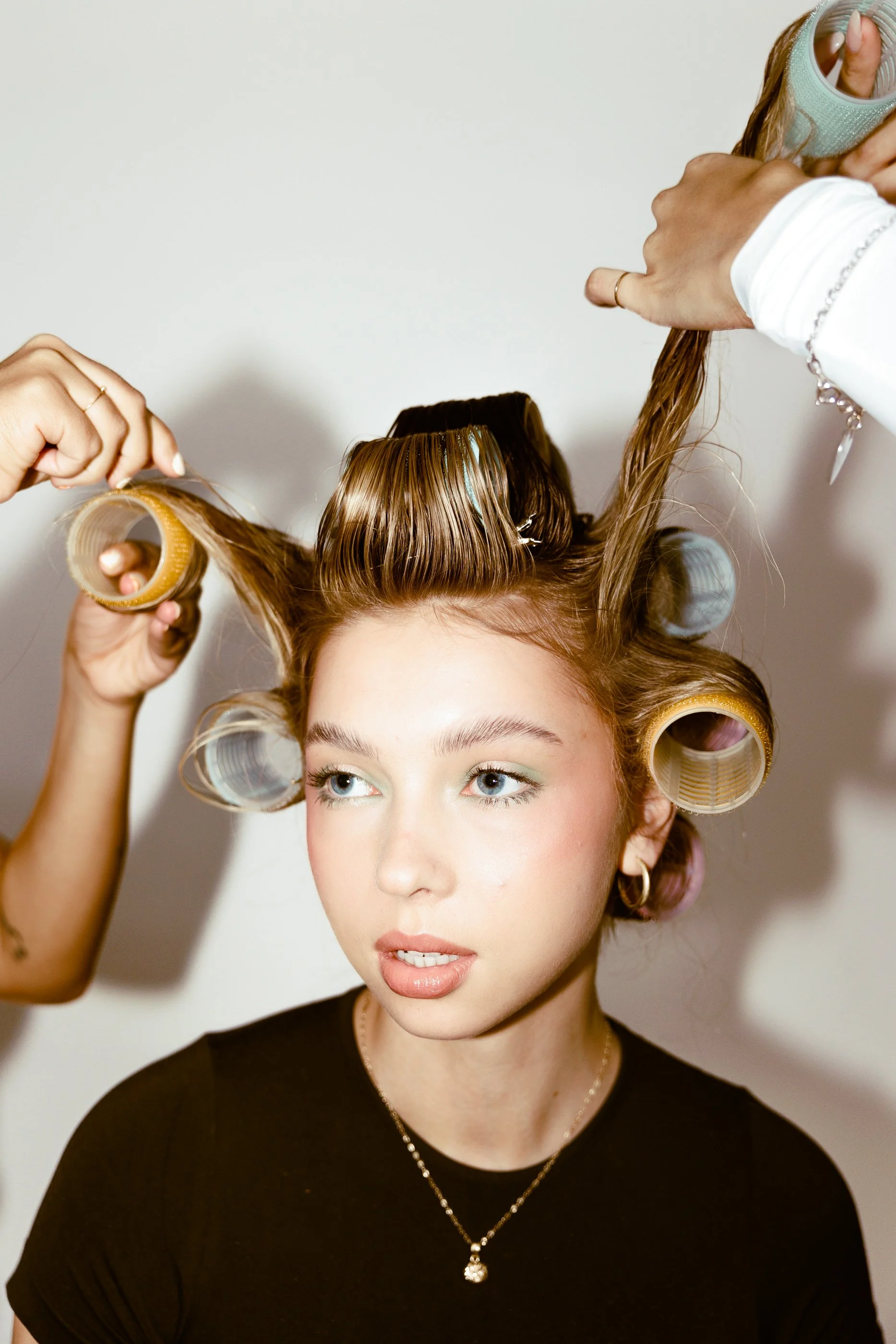 A young woman with Blonde Balayage hair is having her hair styled with rollers while getting ready, possibly for a photoshoot or special event at the Paloma hair salon in Jersey City.