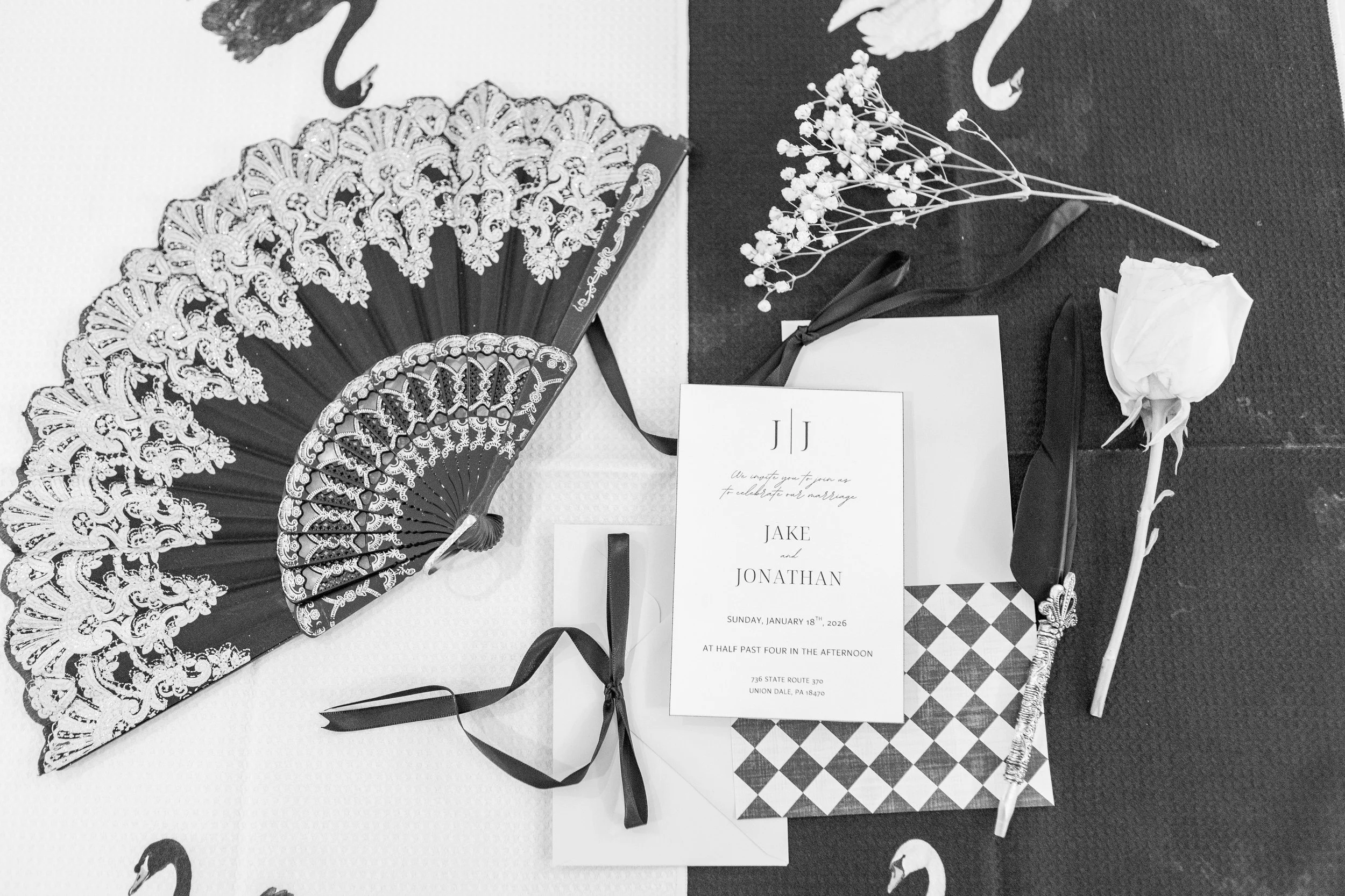 Wedding invitation surrounded by white roses, dried flowers, and decorative fans on a table