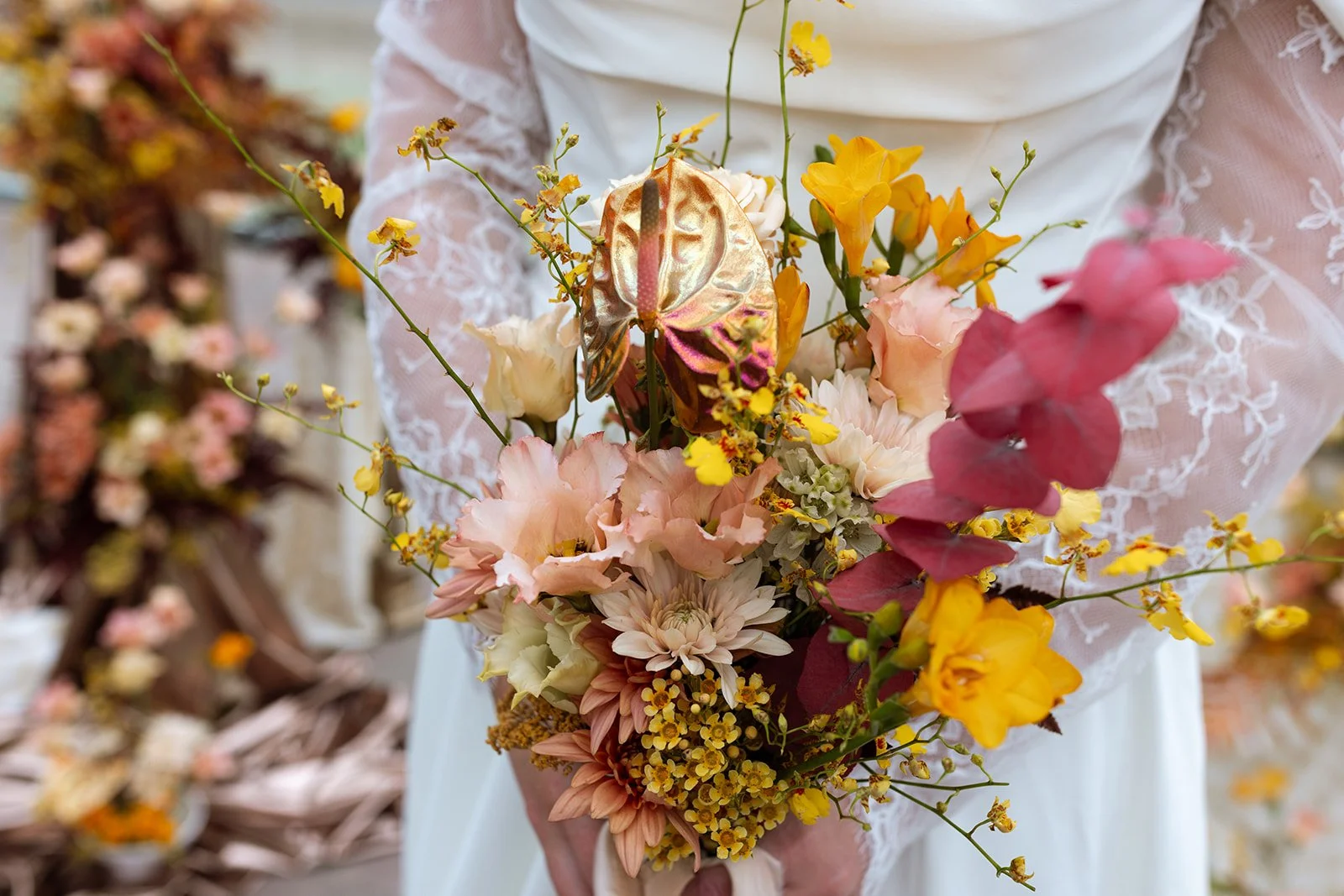 A person in a white lace dress holding a colorful bouquet of flowers and a butterfly-shaped ornament.