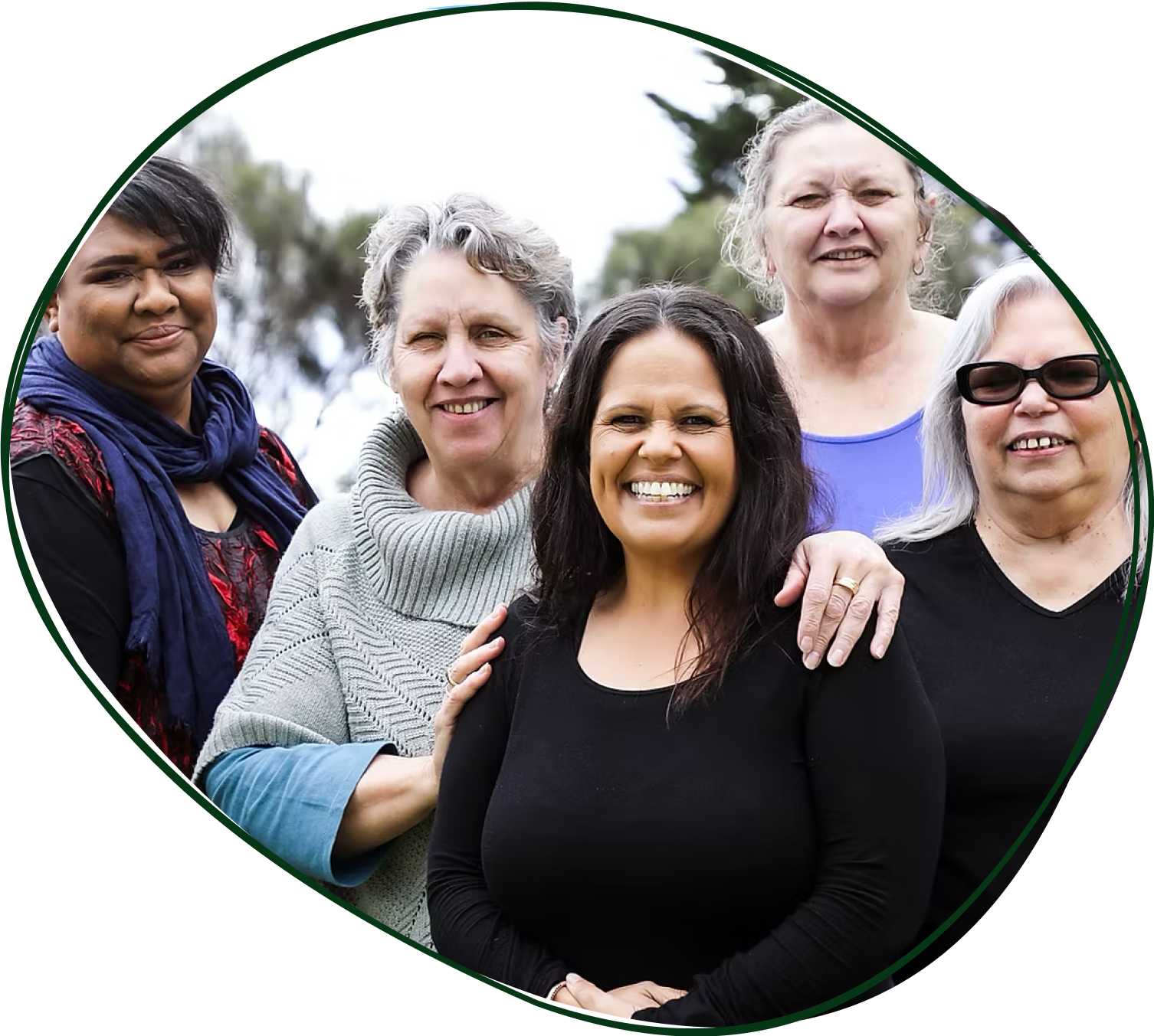 Group of six women outdoors, smiling, standing close together with their arms around each other.