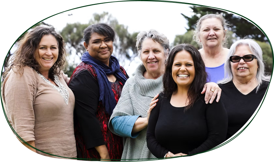 Group of six women smiling outdoors, standing together, with trees and cloudy sky in the background.