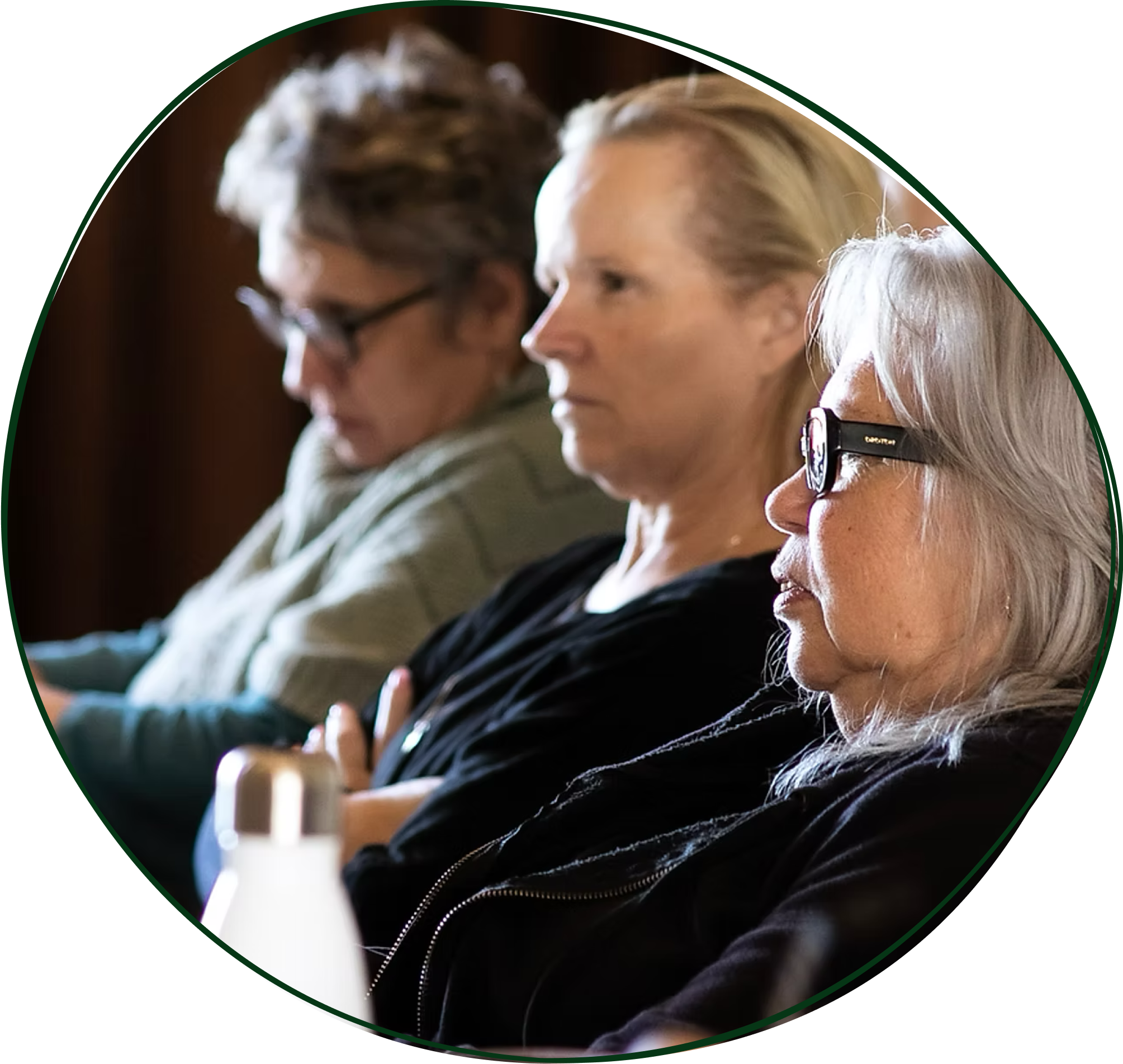 Three women sitting with their eyes closed, possibly sleeping or meditating, in a row indoors.