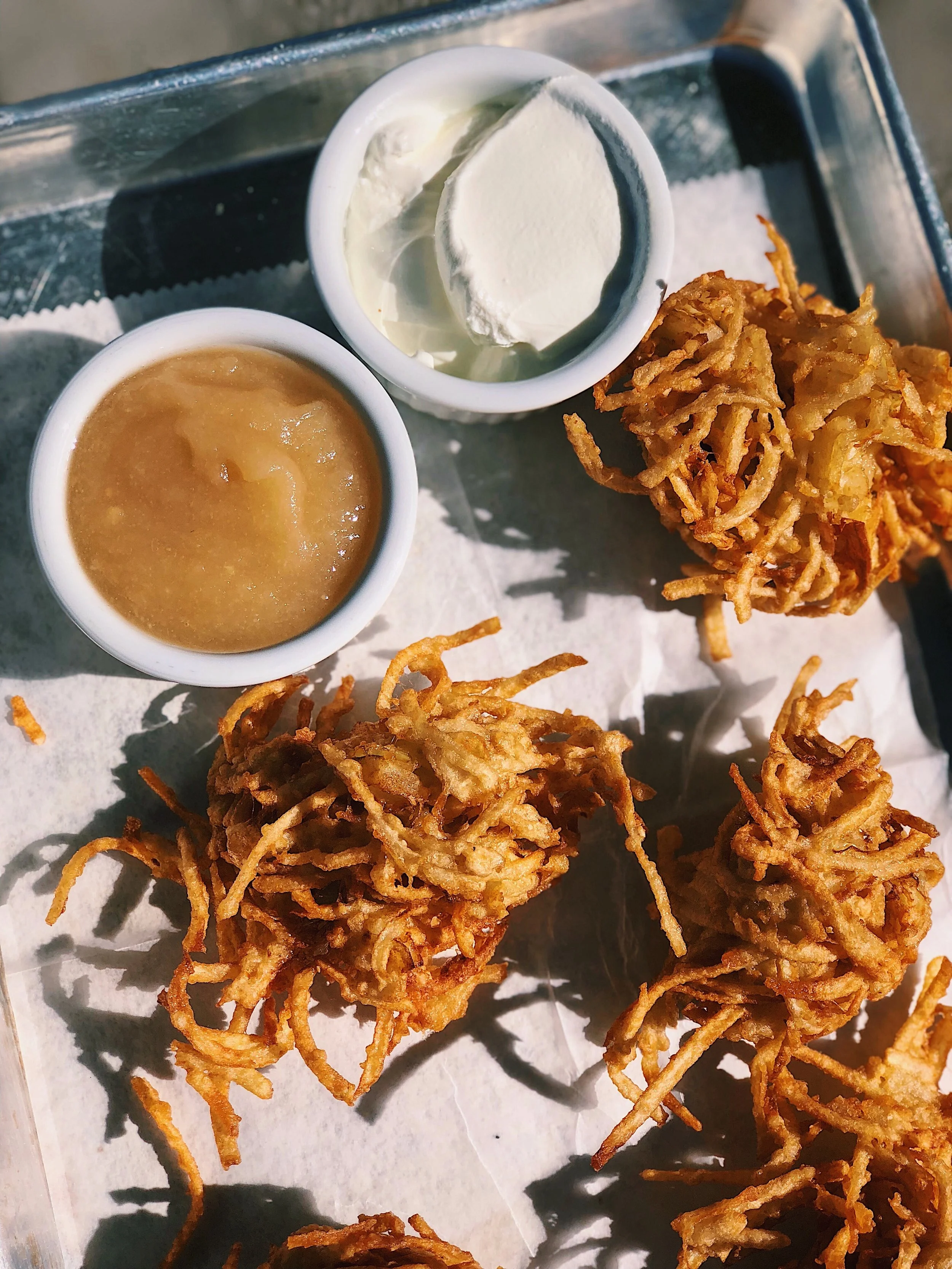Fried onion strings served with two dipping sauces, one creamy and one brown, on a paper-lined tray.