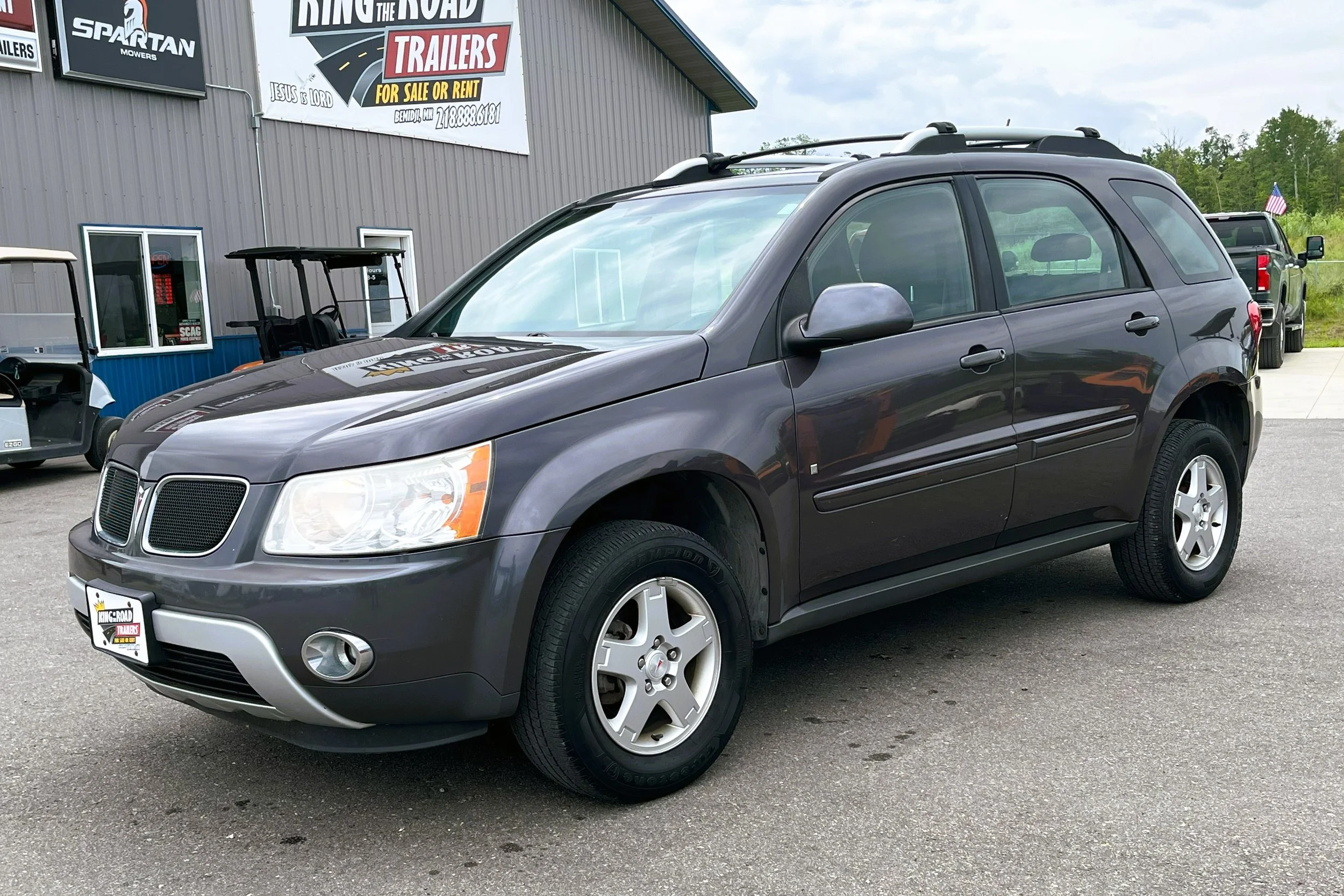Gray Pontiac SUV parked outside a trailer sale lot with a sign that says 'Ring the Road Trailers' in the background.
