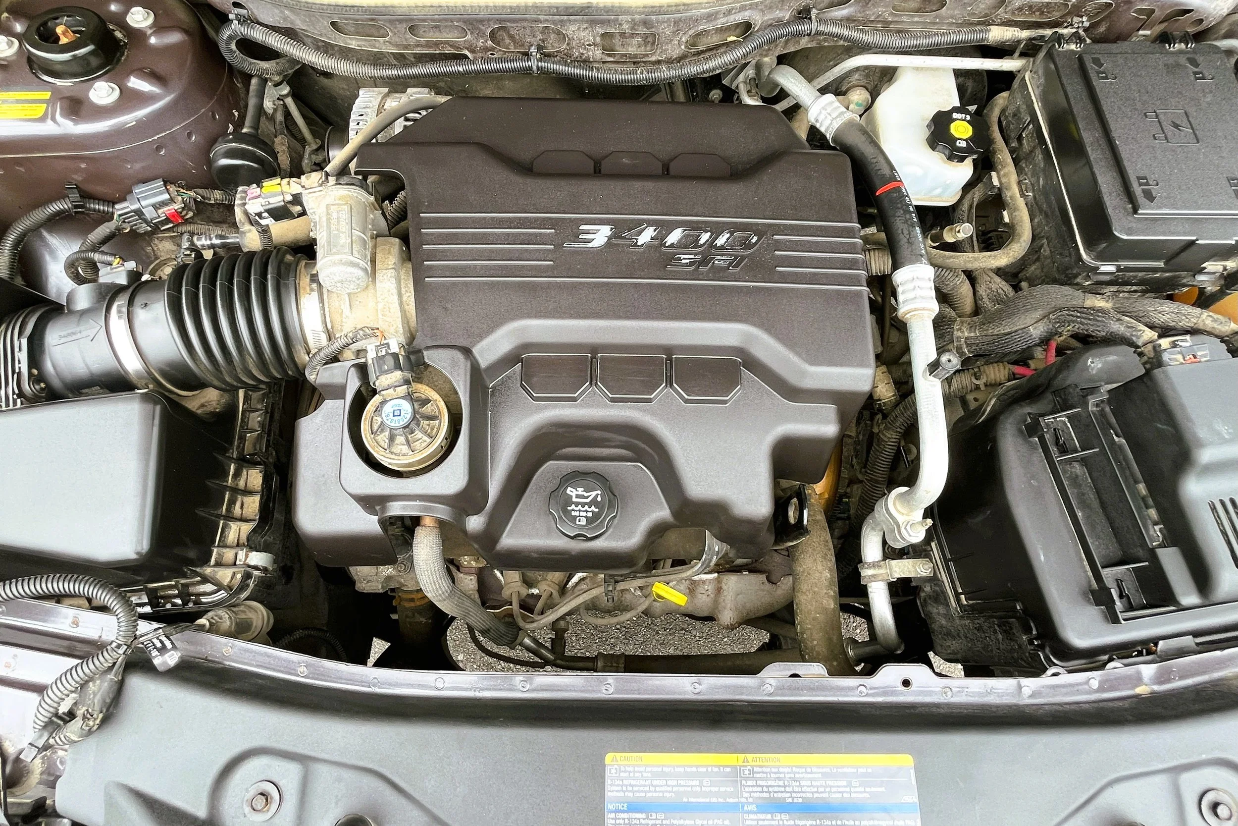 Under the hood of a car showing a 3.4L engine, oil cap, and engine components