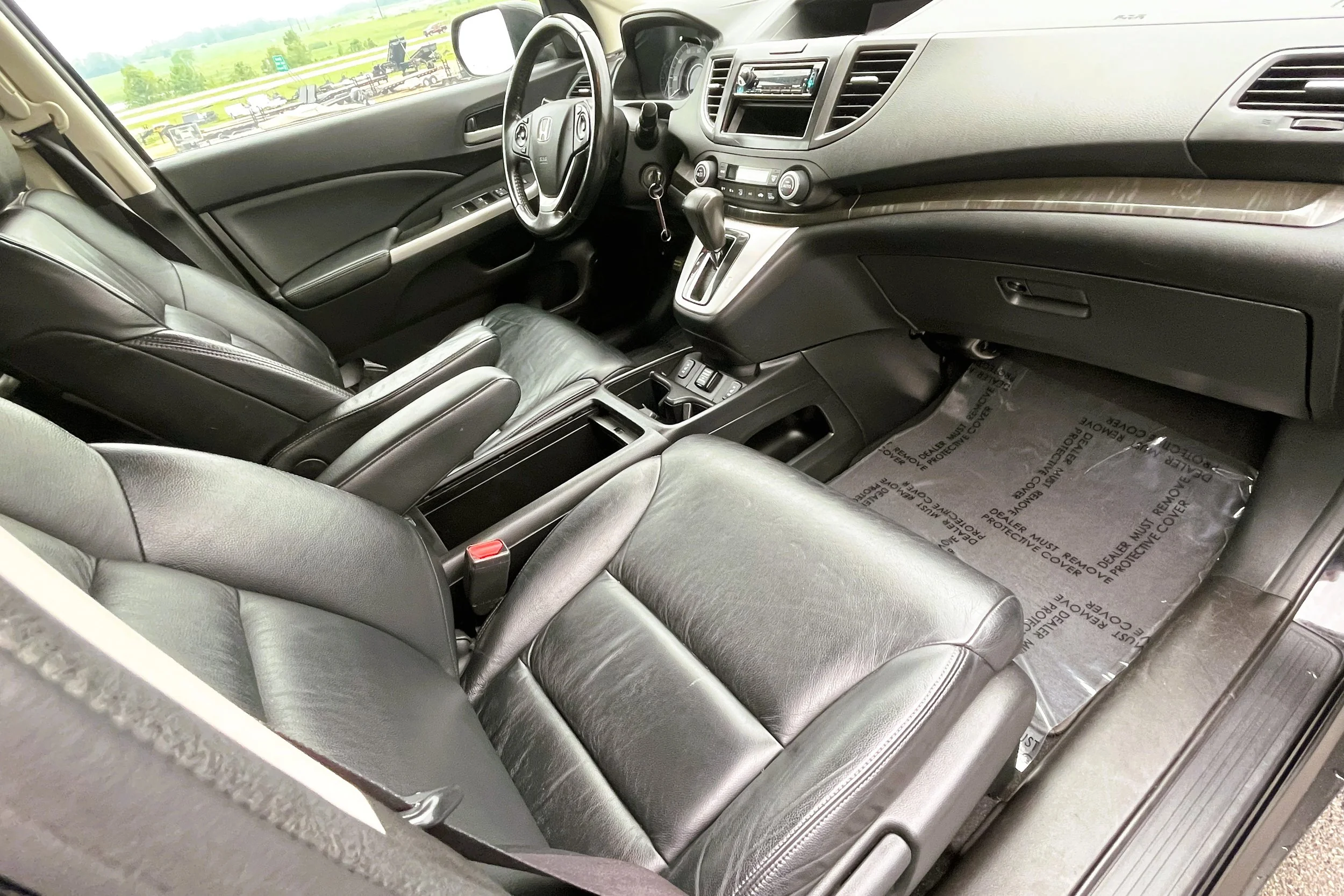 Interior of a car showing two black leather front seats, dashboard, steering wheel, and center console with gear shift, located on a highway with green landscape outside.