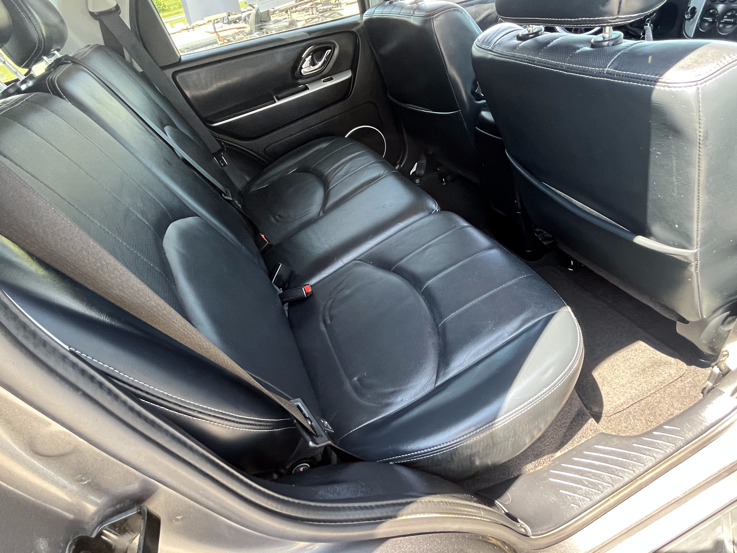The backseat area of a car with black leather seats and seat belts, viewed from the open door.