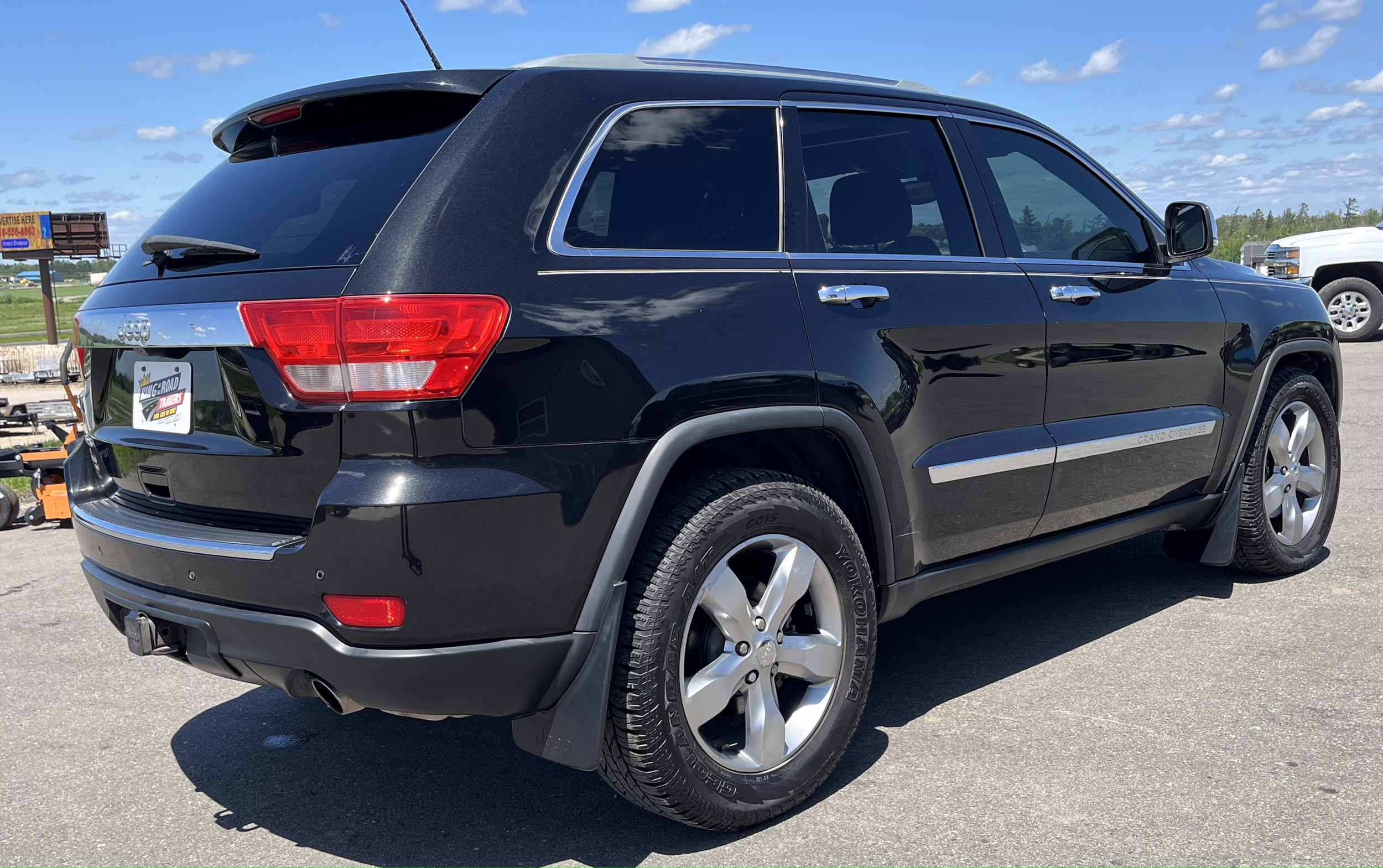 Black Jeep Grand Cherokee parked in an outdoor lot, with a partly cloudy sky in the background.