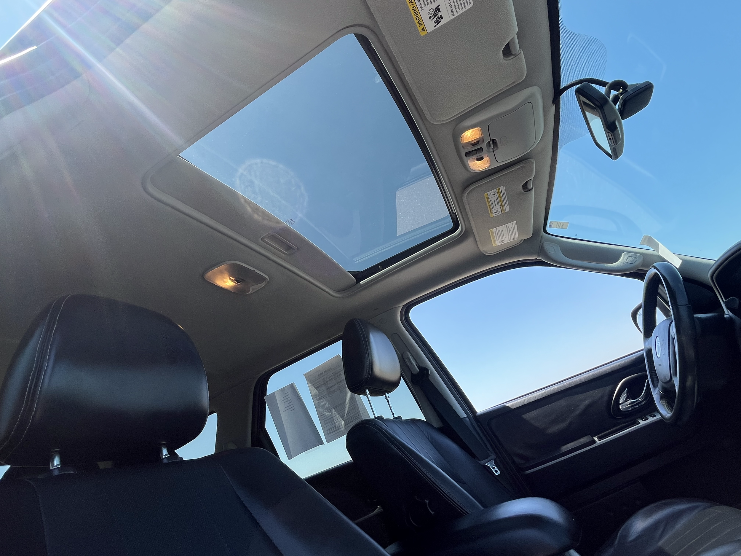 Interior view of a vehicle showing the sunroof, front seats, steering wheel, and dashboard against a clear blue sky.