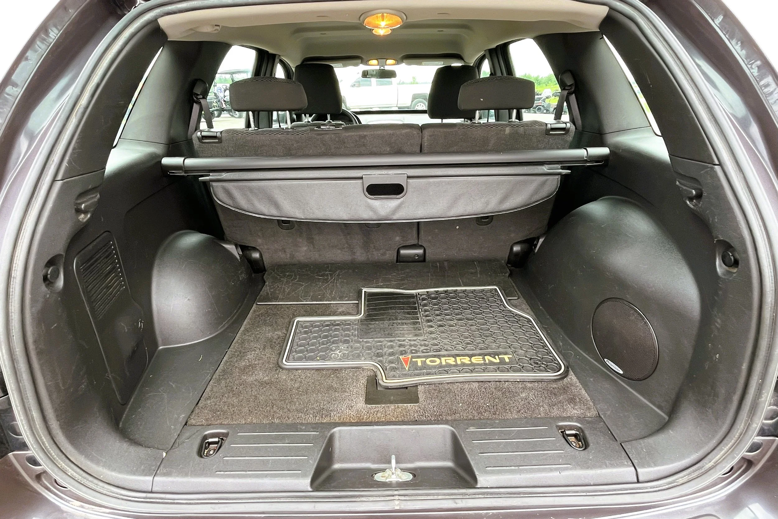 The open trunk of a car showing a cargo space with a black floor mat and a black cargo cover, with three headrests visible in the rear seats.