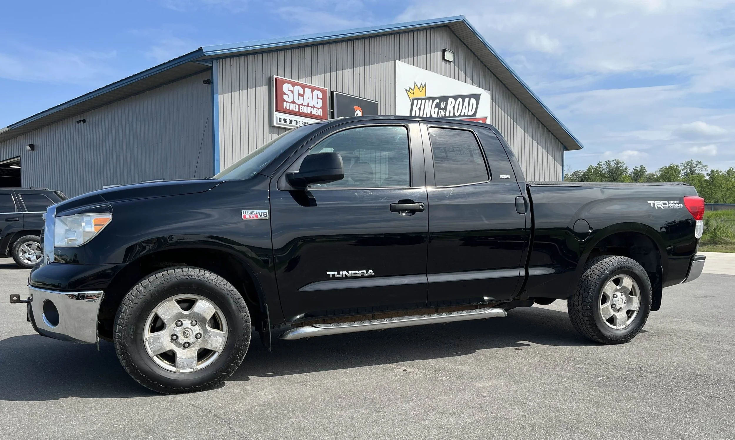 Black Toyota Tundra pickup truck parked in front of a building with signs reading 'SCAG Power Equipment' and 'King of the Road'
