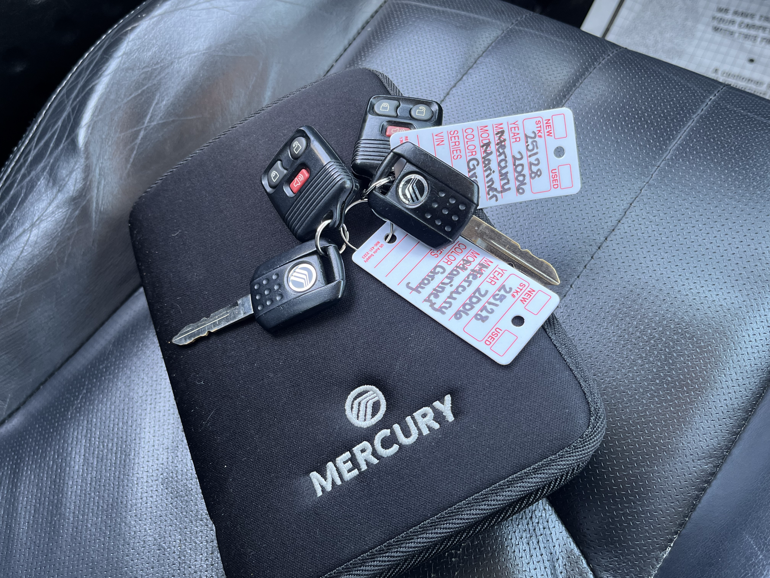 A pair of car keys with remote controls and a black Mercury branded case on a car seat, along with vehicle information tags.